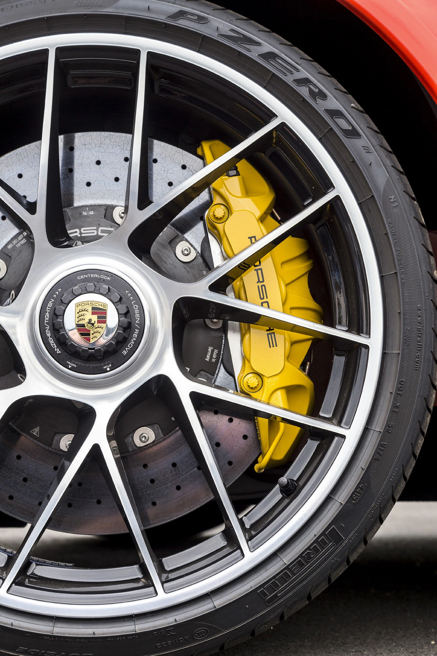 Nahaufnahme eines Autoreifens mit schwarzer Felge, gelber Bremssattel mit "Porsche"-Schriftzug sichtbar, sportliches Design.