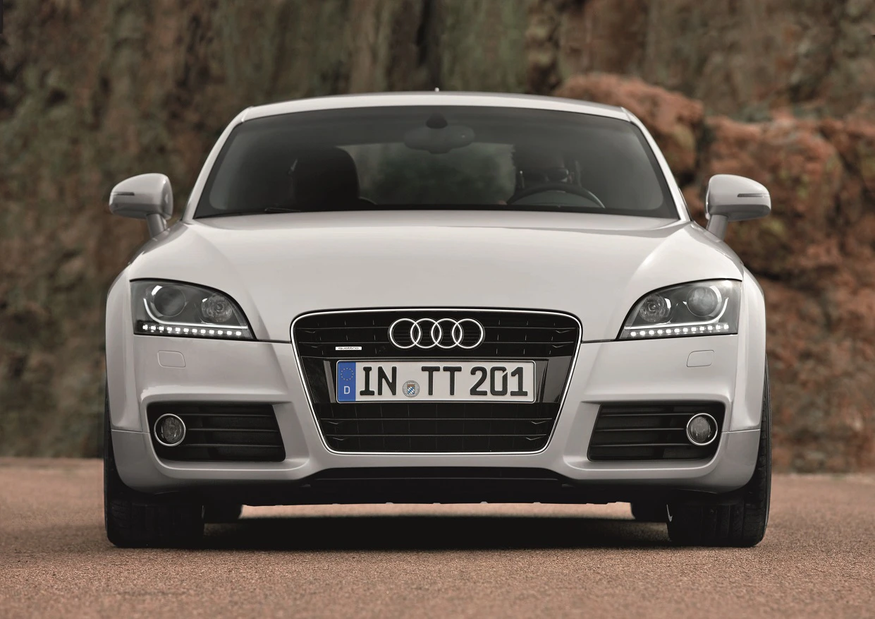 Ein weißer Audi TT von vorne, auf einer Straße vor einem felsigen Hintergrund geparkt. Das Kennzeichen zeigt "IN TT 201".