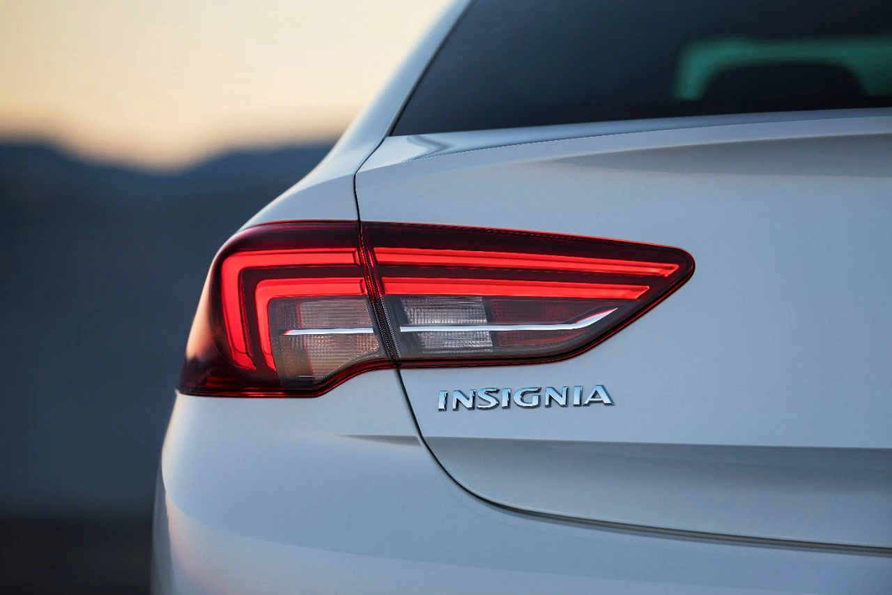 Rückansicht eines weißen Autos mit leuchtendem Hecklicht und dem Schriftzug "Insignia".