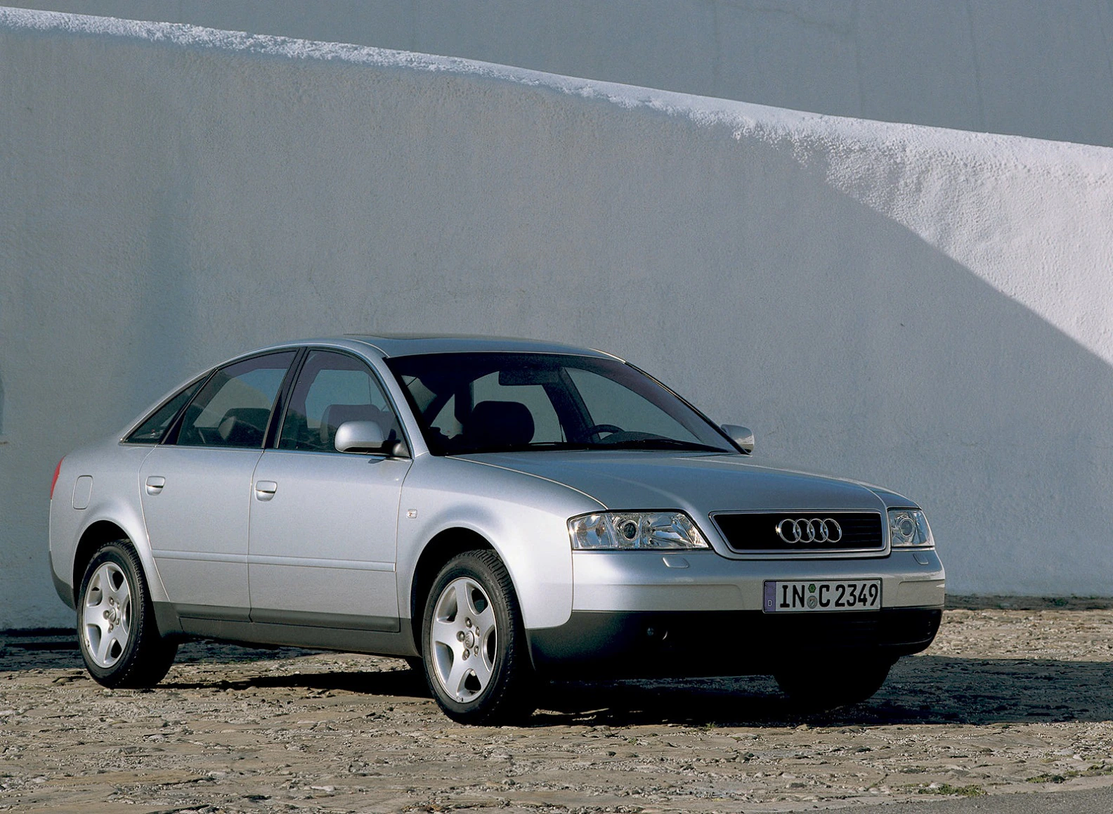 Silberner Audi A6 Limousine vor einer weißen Wand geparkt. Sunflair auf der Motorhaube, sauber und glänzend. Vorderansicht von leicht links.