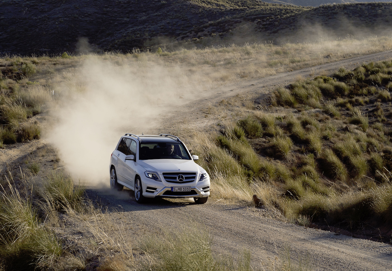 SUV auf staubiger, unbefestigter Straße in hügeliger Landschaft. Staub wirbelt hinter dem Fahrzeug auf.