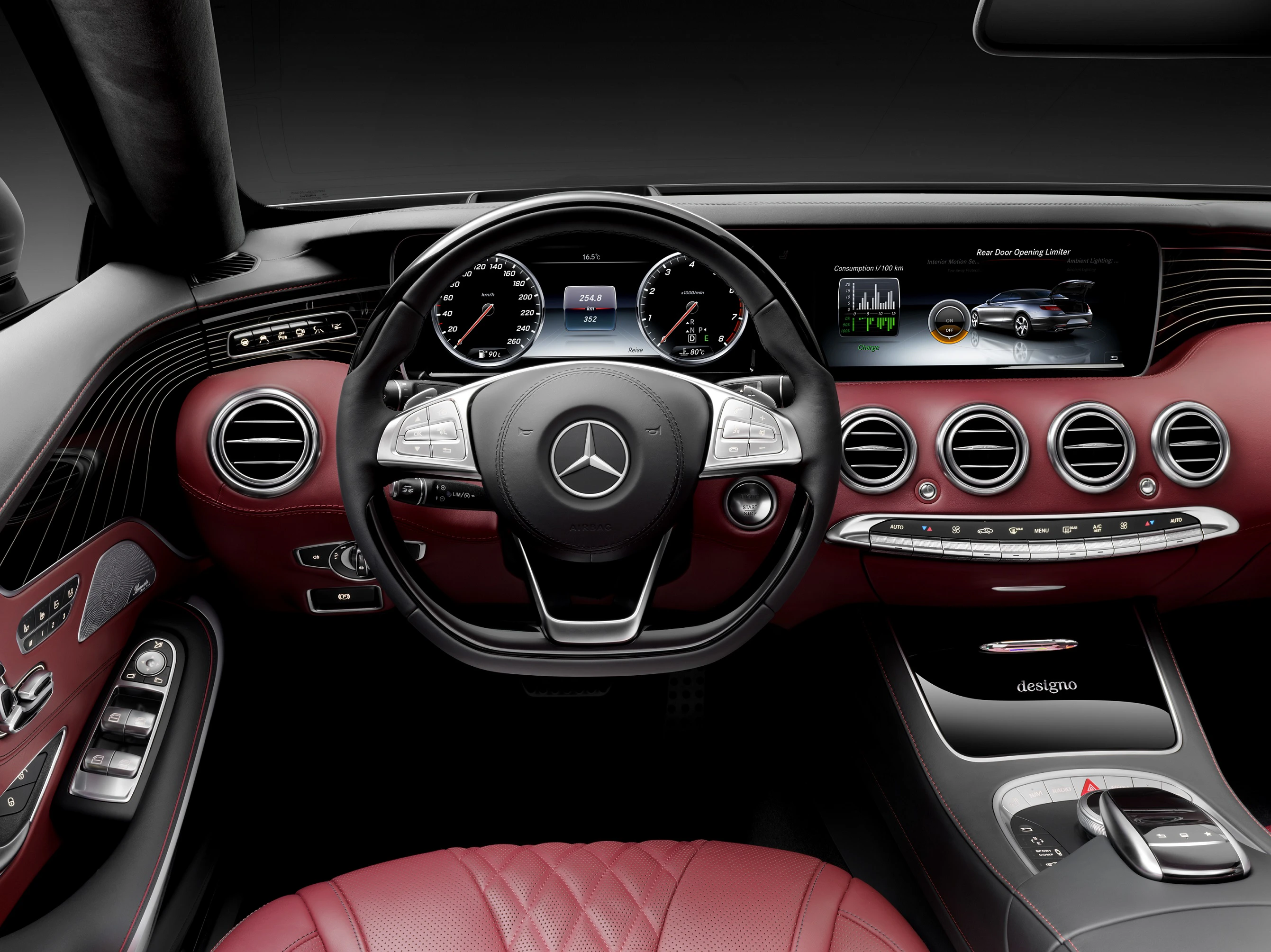Innenraum eines Mercedes mit rotem Leder, Lenkrad mit Mercedes-Logo, digitalem Display und luxuriösen Details.