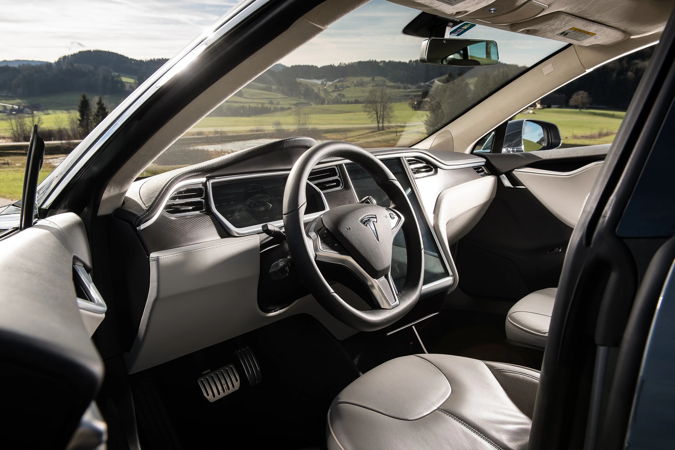 Innenraum eines modernen Autos mit stilvollem Lenkrad und Lederpolstern. Durch die Fenster ist eine ländliche Landschaft zu sehen.