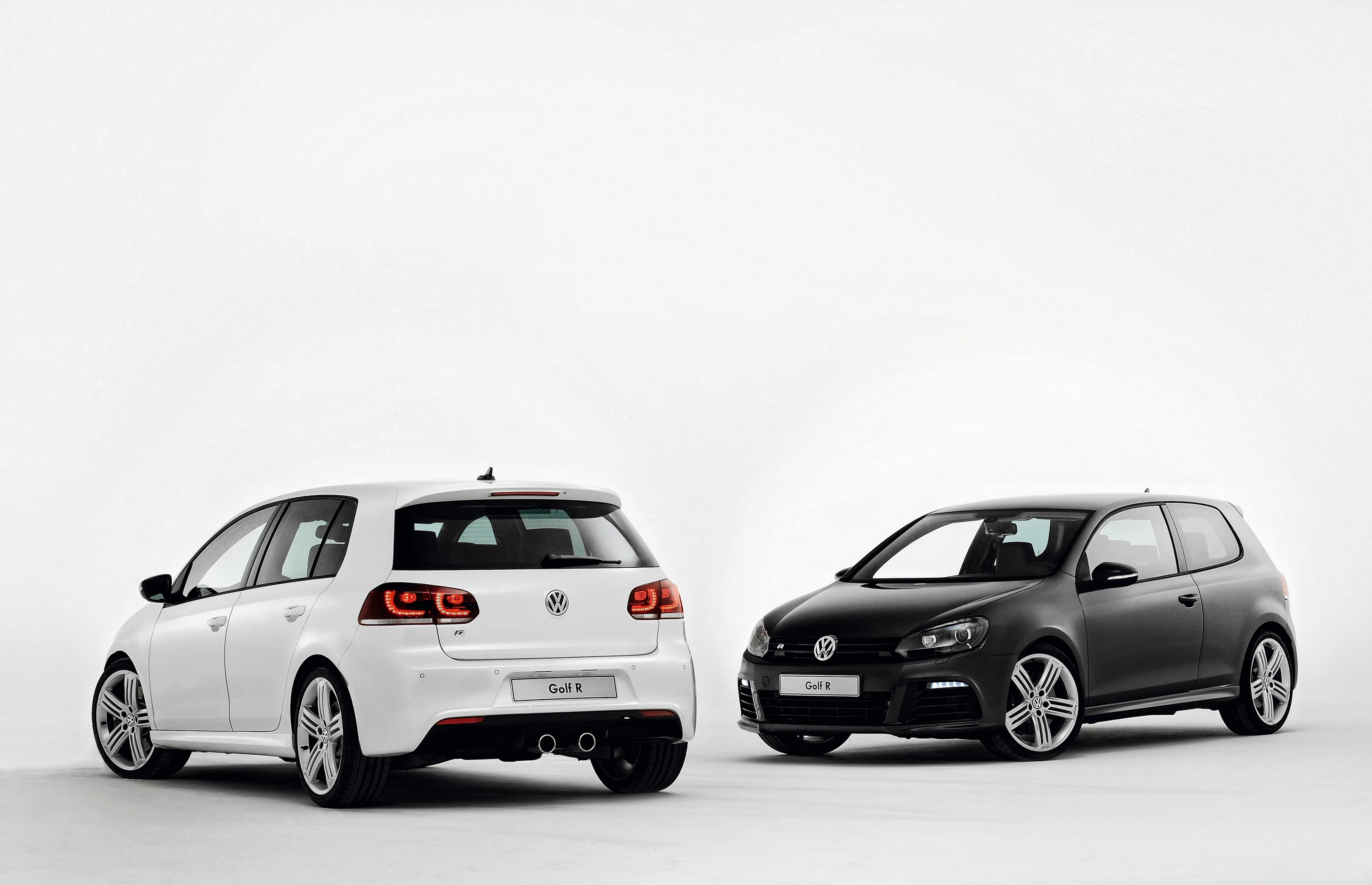 Zwei VW Golf R: ein weißer und ein schwarzer, beide sportlich designt, auf hellem Hintergrund nebeneinander platziert.
