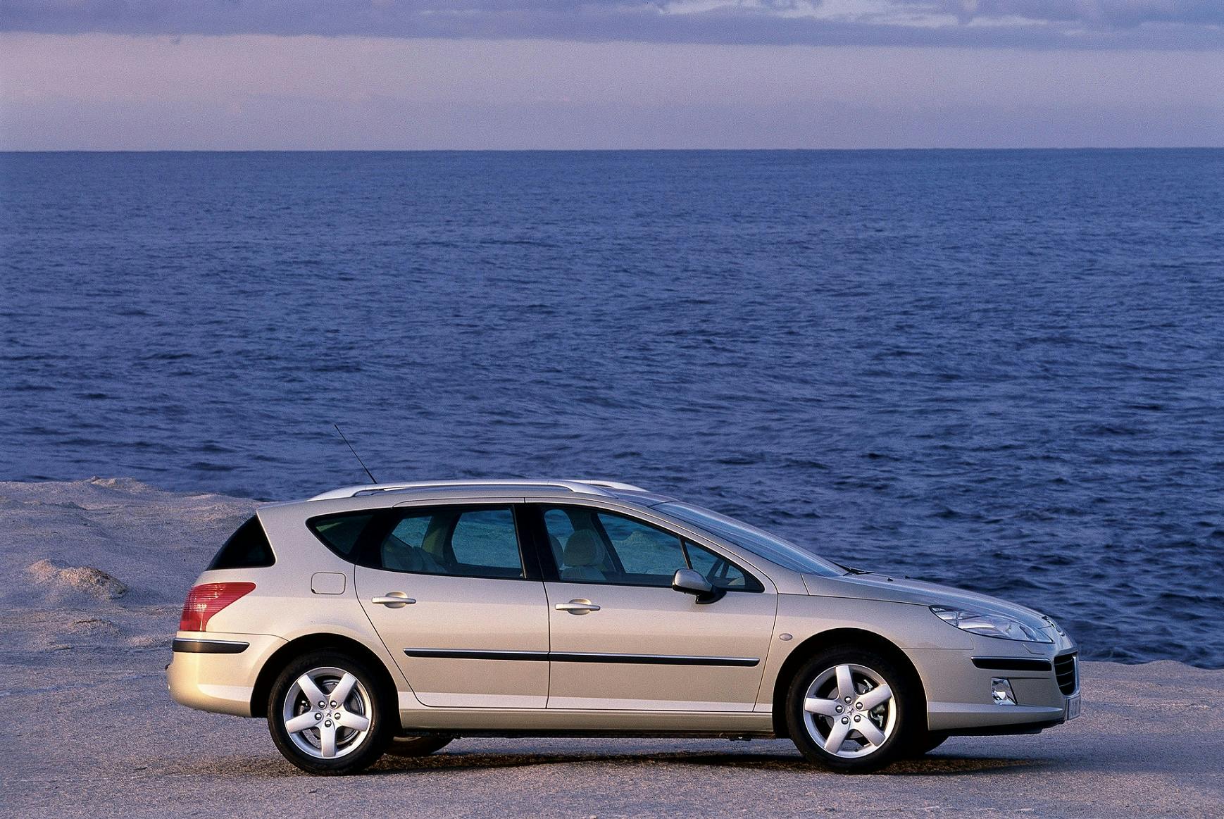 Silberner Kombi geparkt auf felsigem Ufer vor einem ruhigen Meer und blauem Himmel im Hintergrund.
