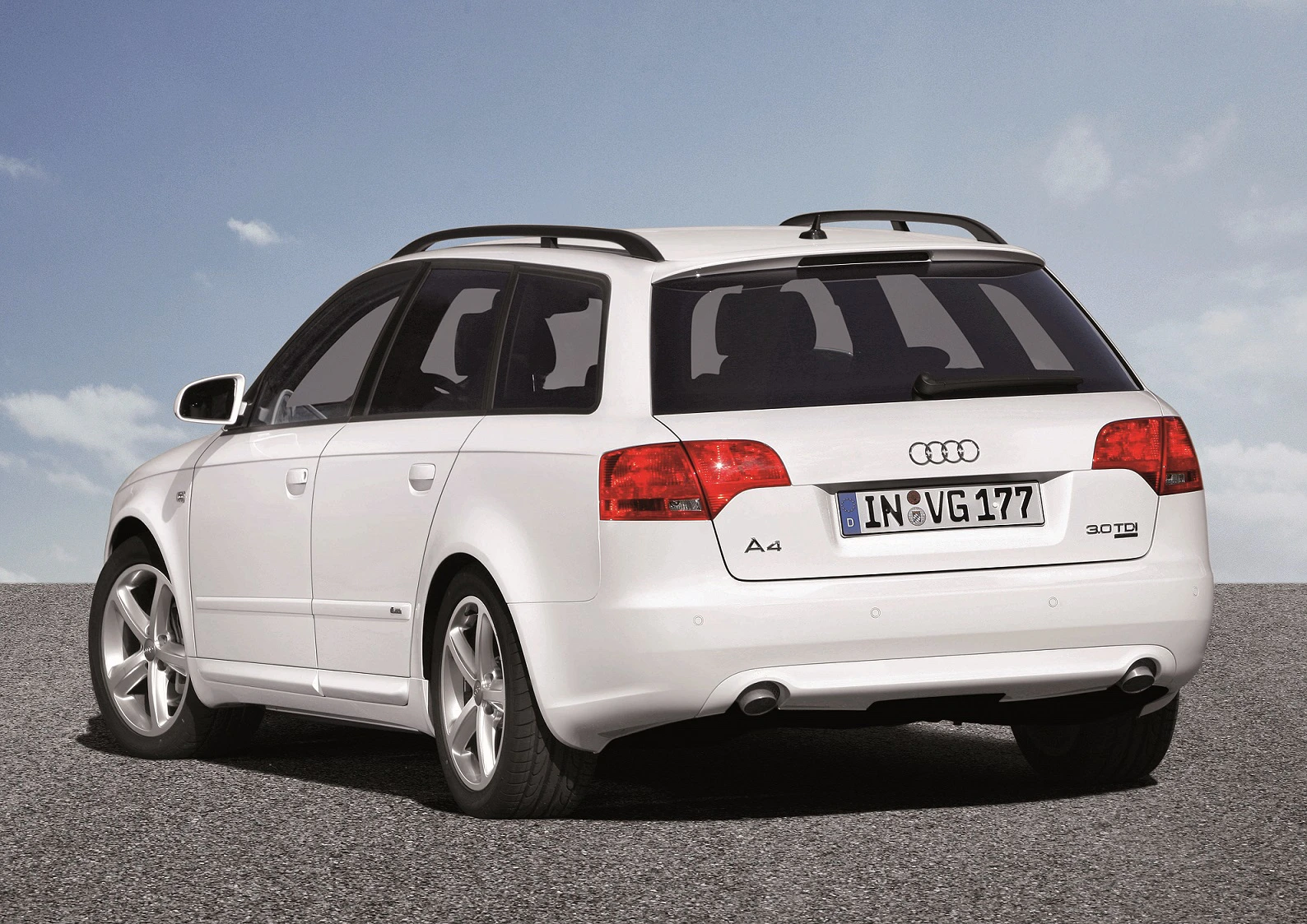 Weißer Audi A4 Kombi auf grauem Asphalt, von hinten fotografiert. Dachgepäckträger und klarer Himmel im Hintergrund.