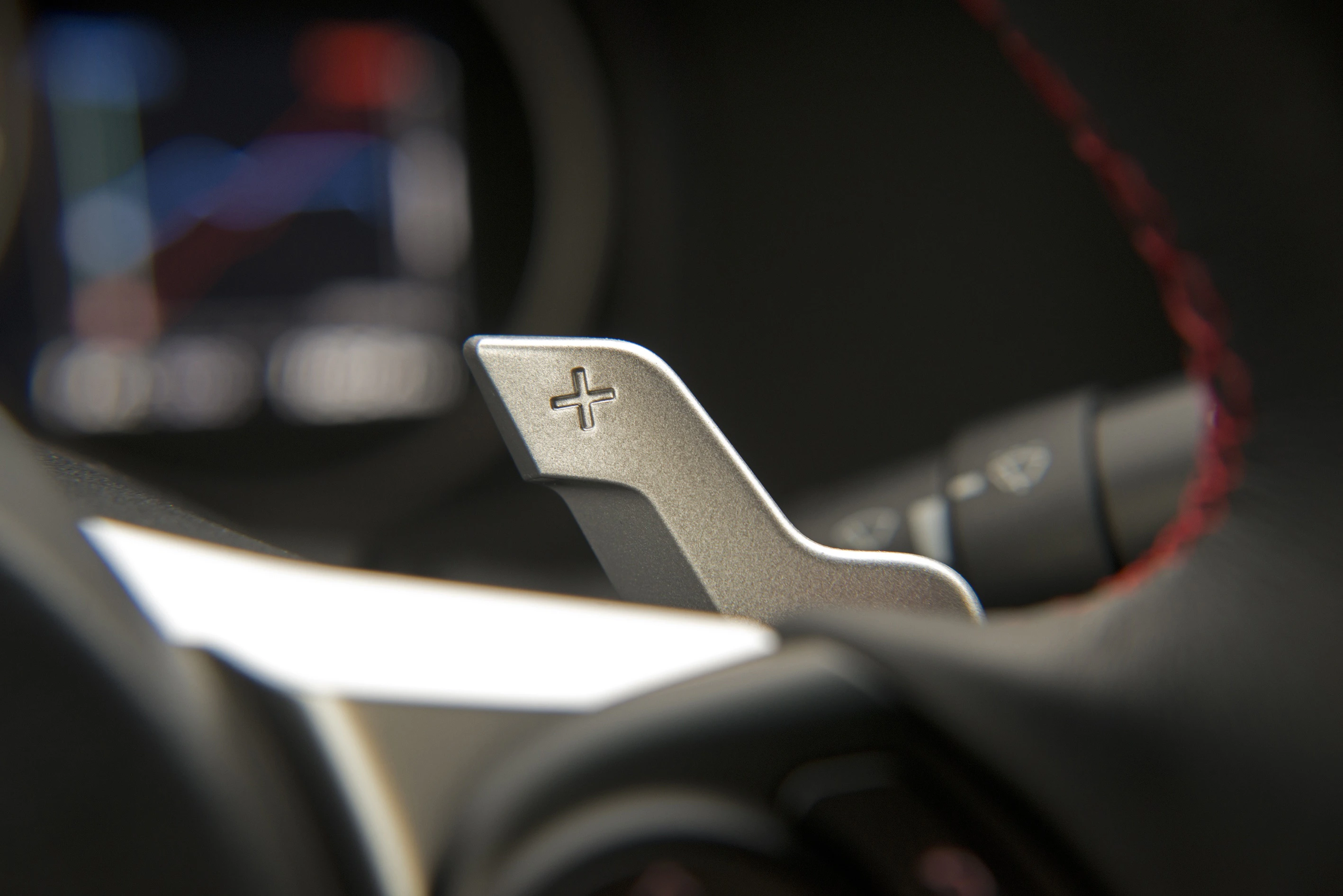 Nahaufnahme eines Schaltwippens im Auto mit einem Plus-Zeichen auf der Oberseite, unscharfer Hintergrund mit instrumentellem Display.