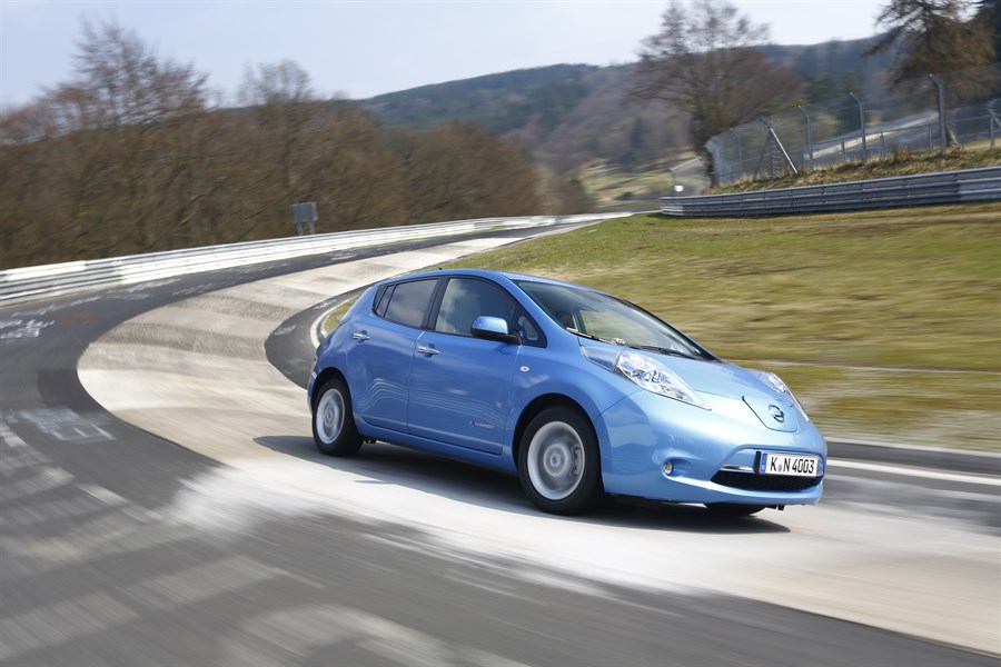Blauer Kleinwagen fährt schnell auf einer kurvenreichen Rennstrecke durch eine bewaldete Landschaft.