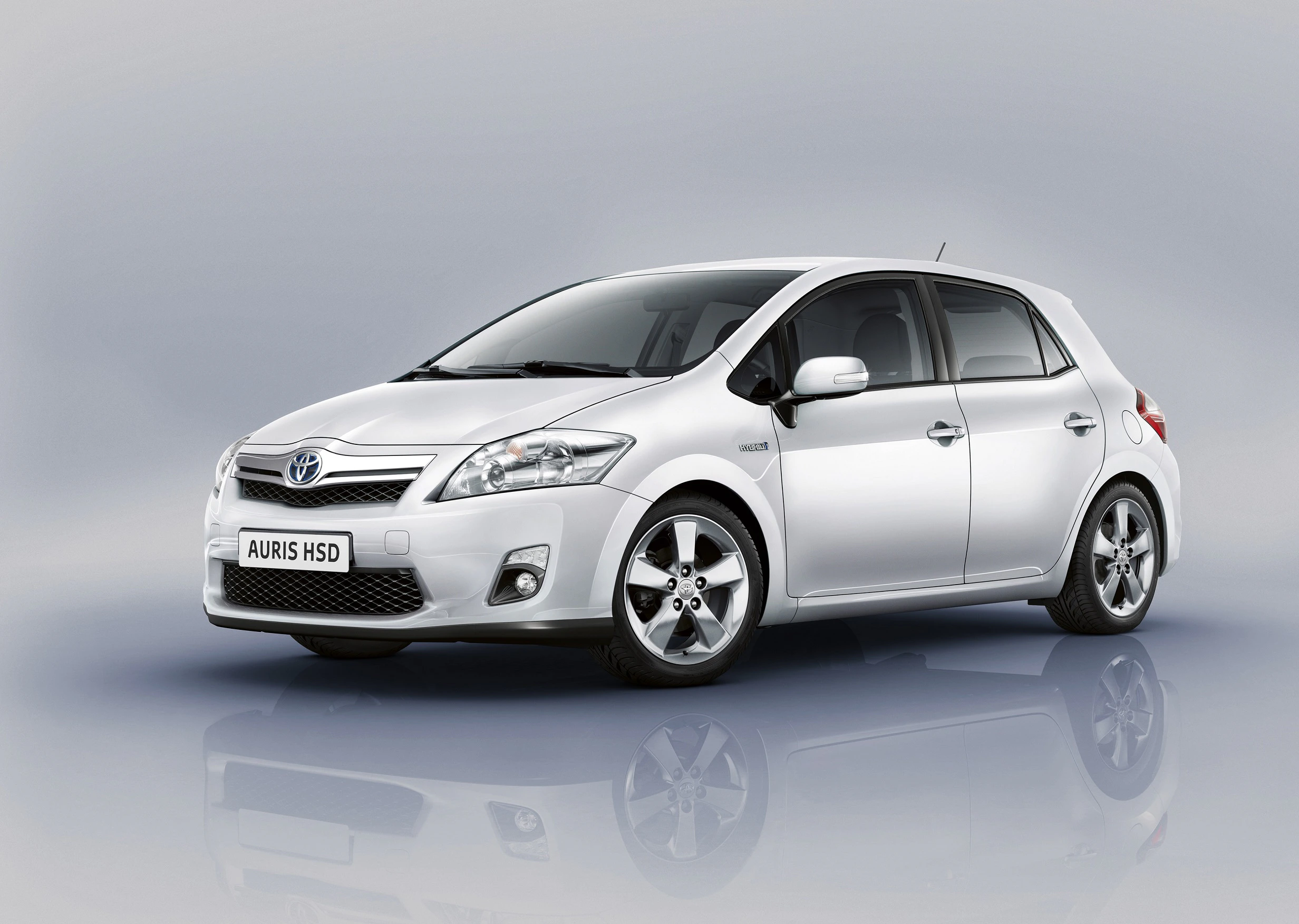 Silberner Toyota Auris HSD, seitlich fotografiert, auf grauem Hintergrund. Fünftüriges Hybridfahrzeug mit markantem Design.