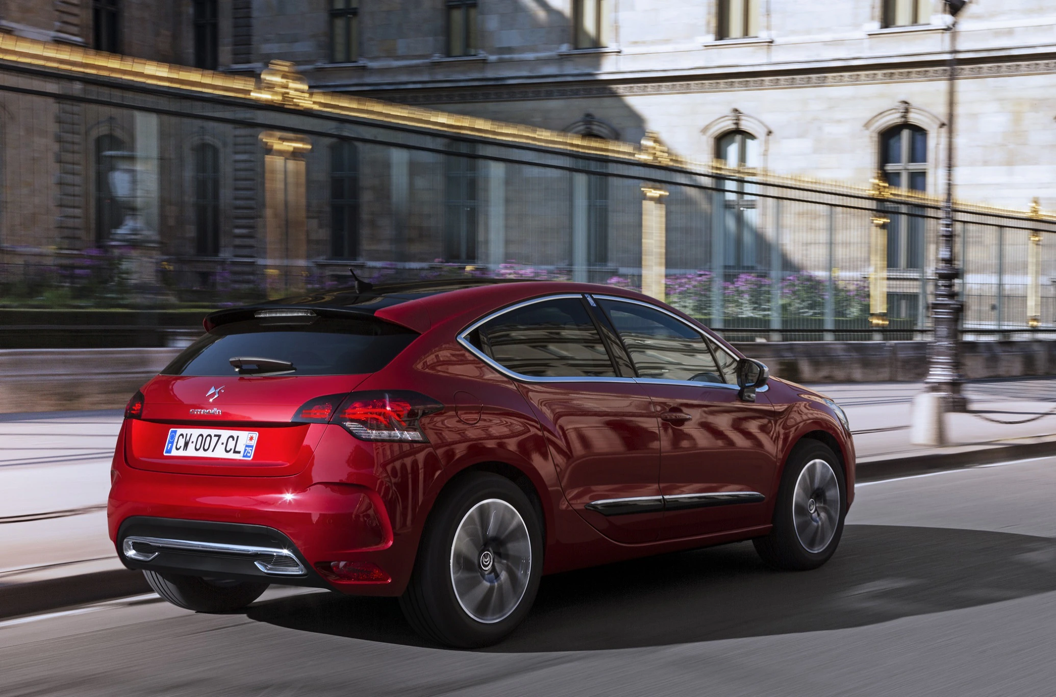 Roter Citroën DS4 fährt auf städtischer Straße mit historischer Architektur im Hintergrund.
