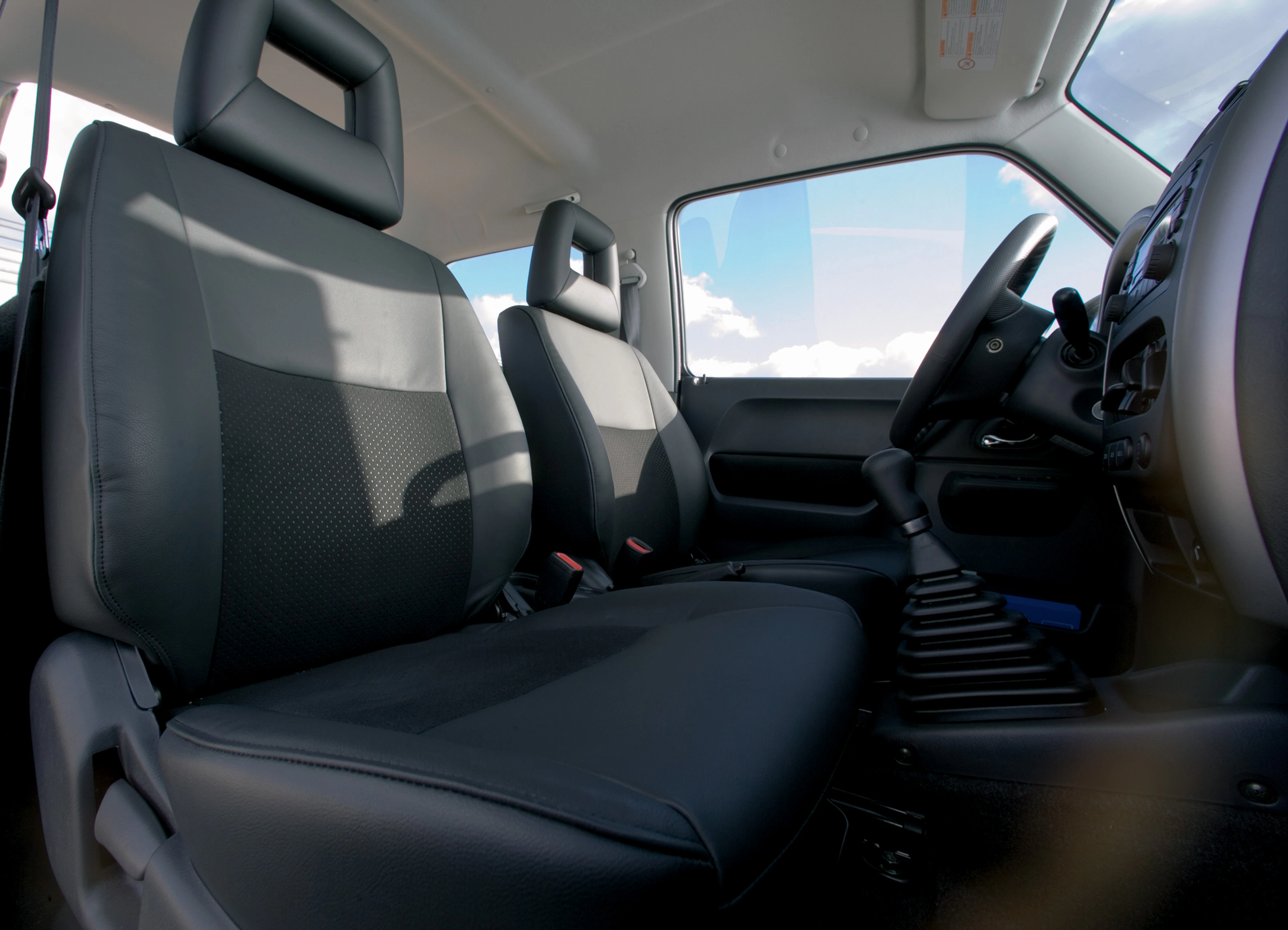 Innenraum eines Autos mit schwarzen Ledersitzen und manueller Schaltung, Sonnenlicht fällt durch die Fenster.