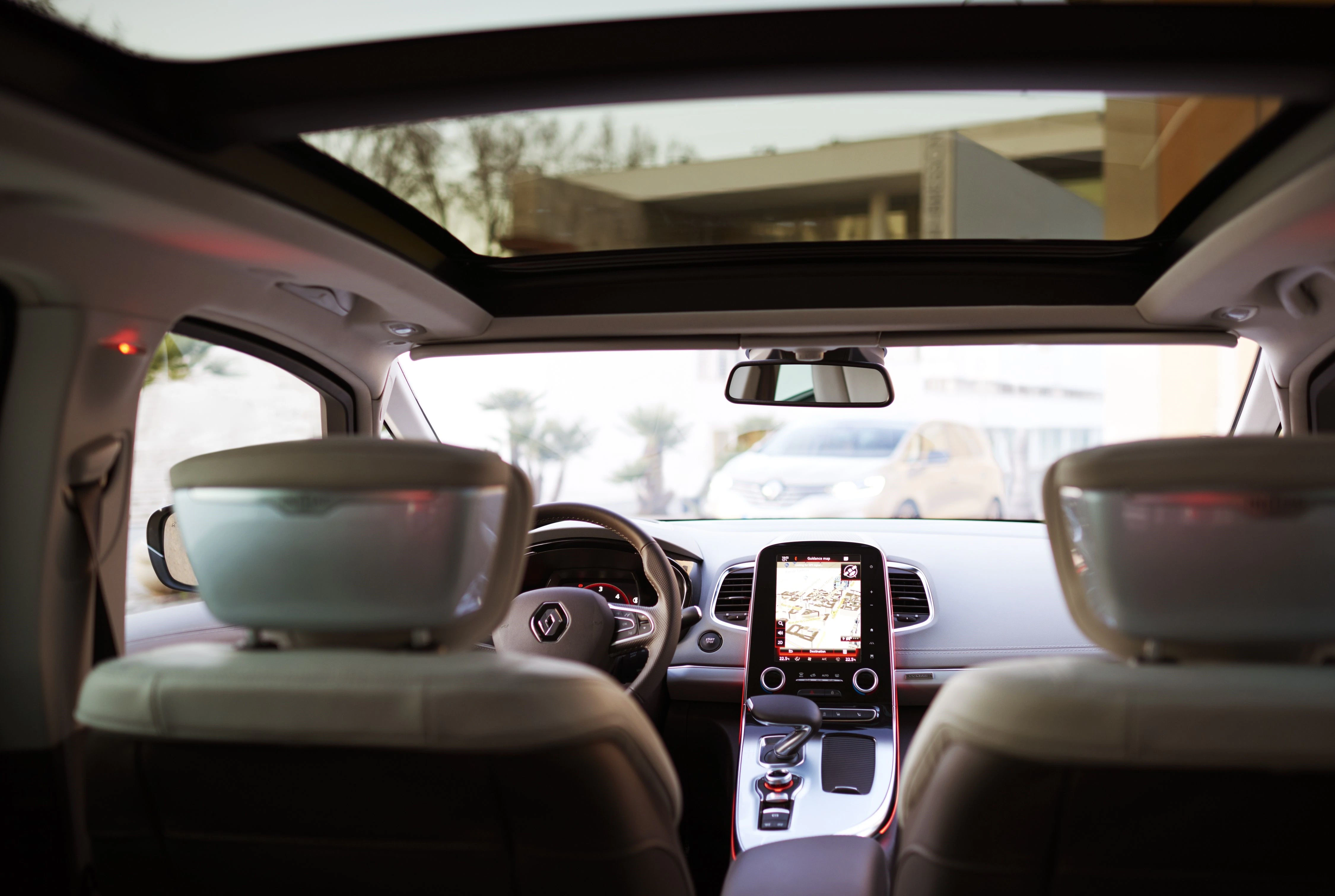 Innenraum eines Autos mit Panoramadach, moderner Mittelkonsole und Touchscreen-Display, Blick aus der Rückbank auf die Straße durch die Windschutzscheibe.