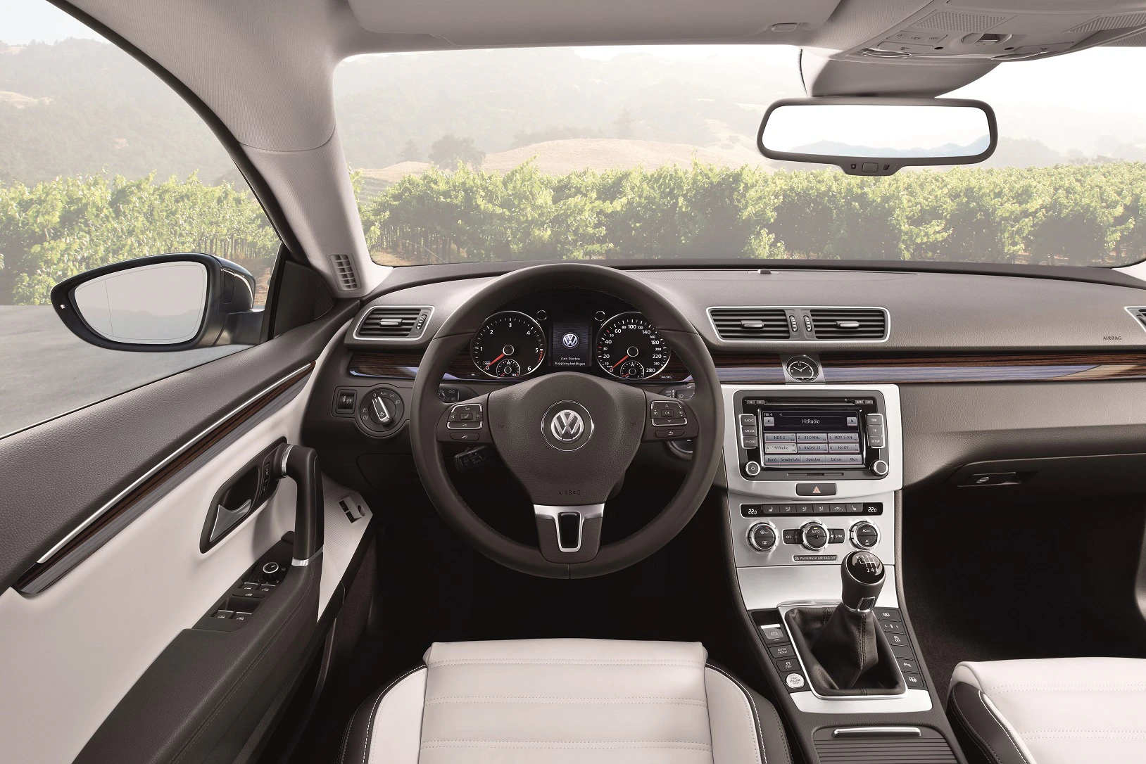 Innenraum eines VW-Autos mit Lenkrad, Armaturenbrett und Schaltknüppel, Blick nach draußen auf eine grüne Landschaft.