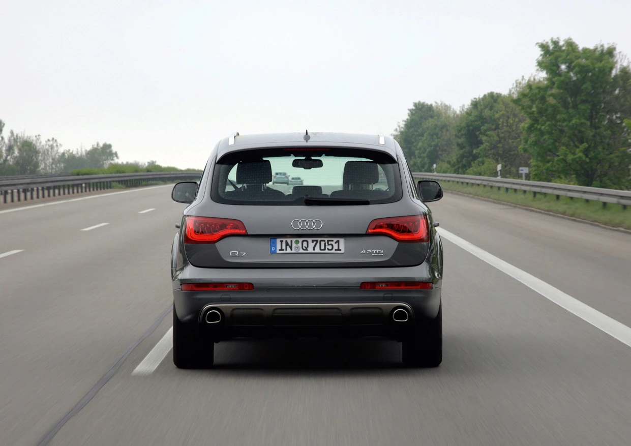 Audi Q5 fährt auf einer Autobahn, umgeben von Bäumen und grauem Himmel. Fahrzeug von hinten sichtbar.