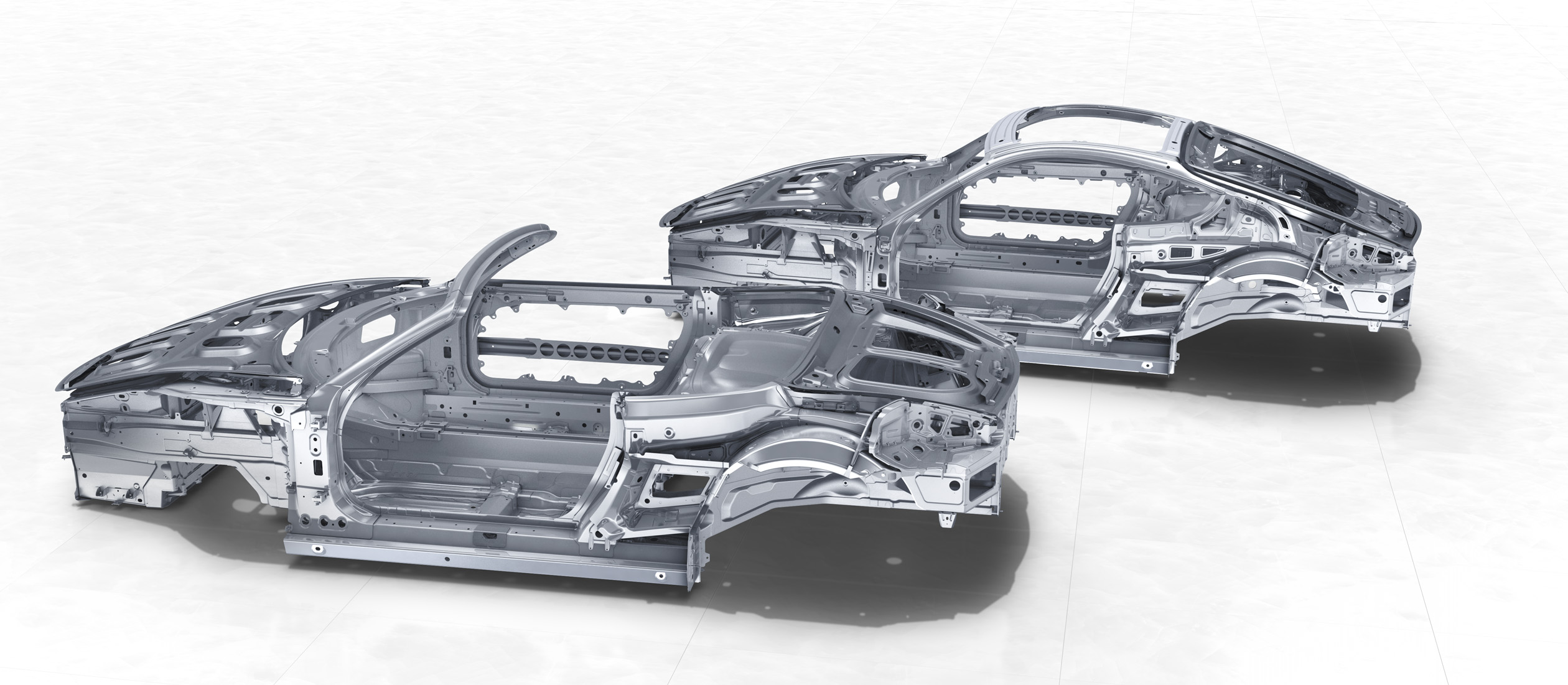 Zwei silberne Autokarosserien ohne Räder und Motor stehen auf hellem Boden, nebeneinander platziert.