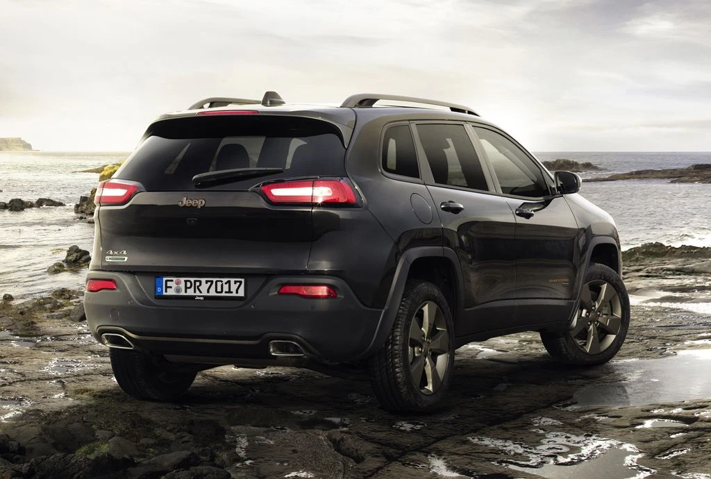 Schwarzer Jeep Cherokee parkt auf felsigem Strand neben dem Meer unter bewölktem Himmel. Rückseite und rechte Seite des Fahrzeugs sichtbar.
