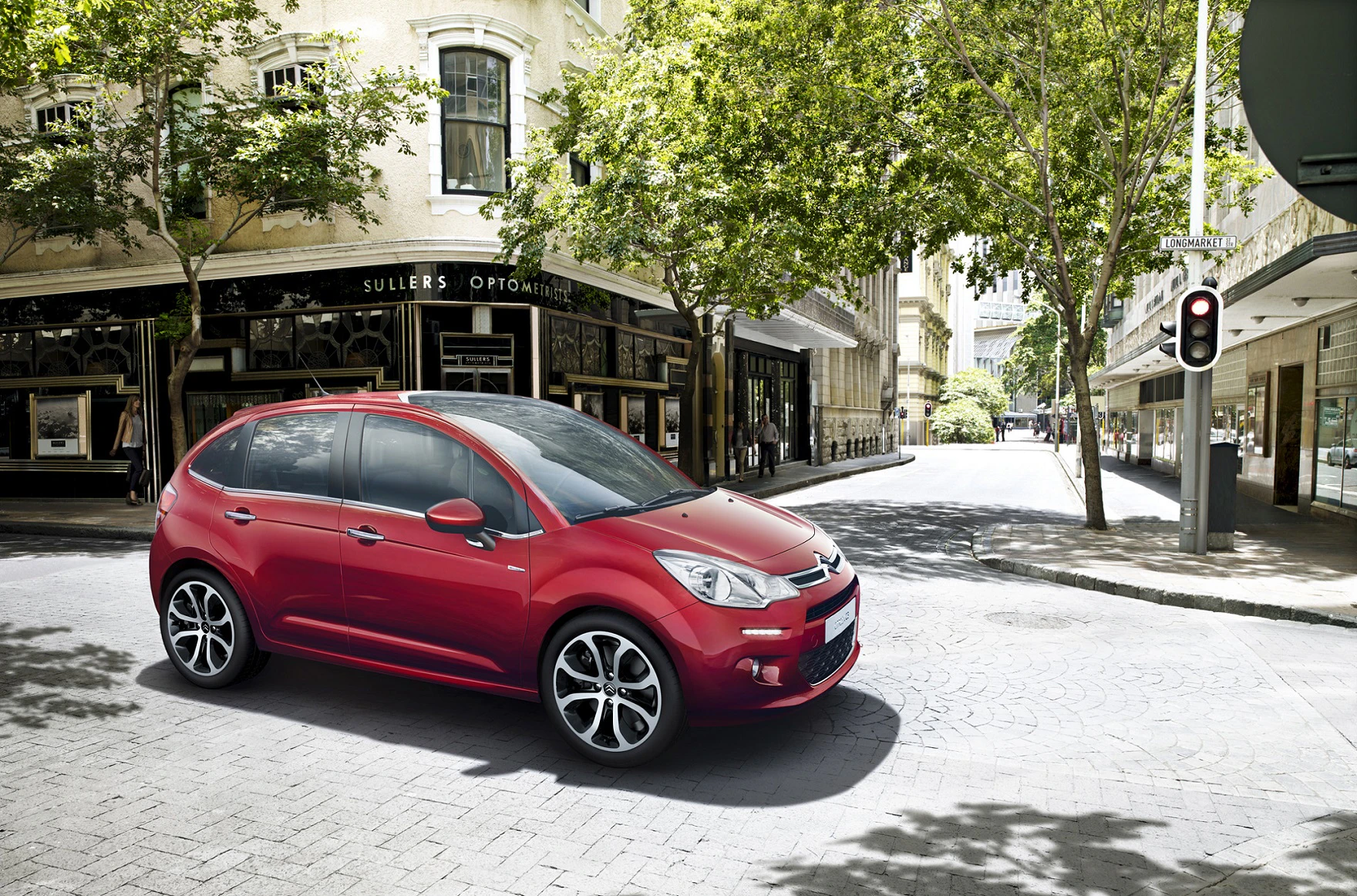 Roter Citroën C3 parkt auf sonniger Stadtstraße vor einem Geschäft mit Bäumen im Hintergrund.