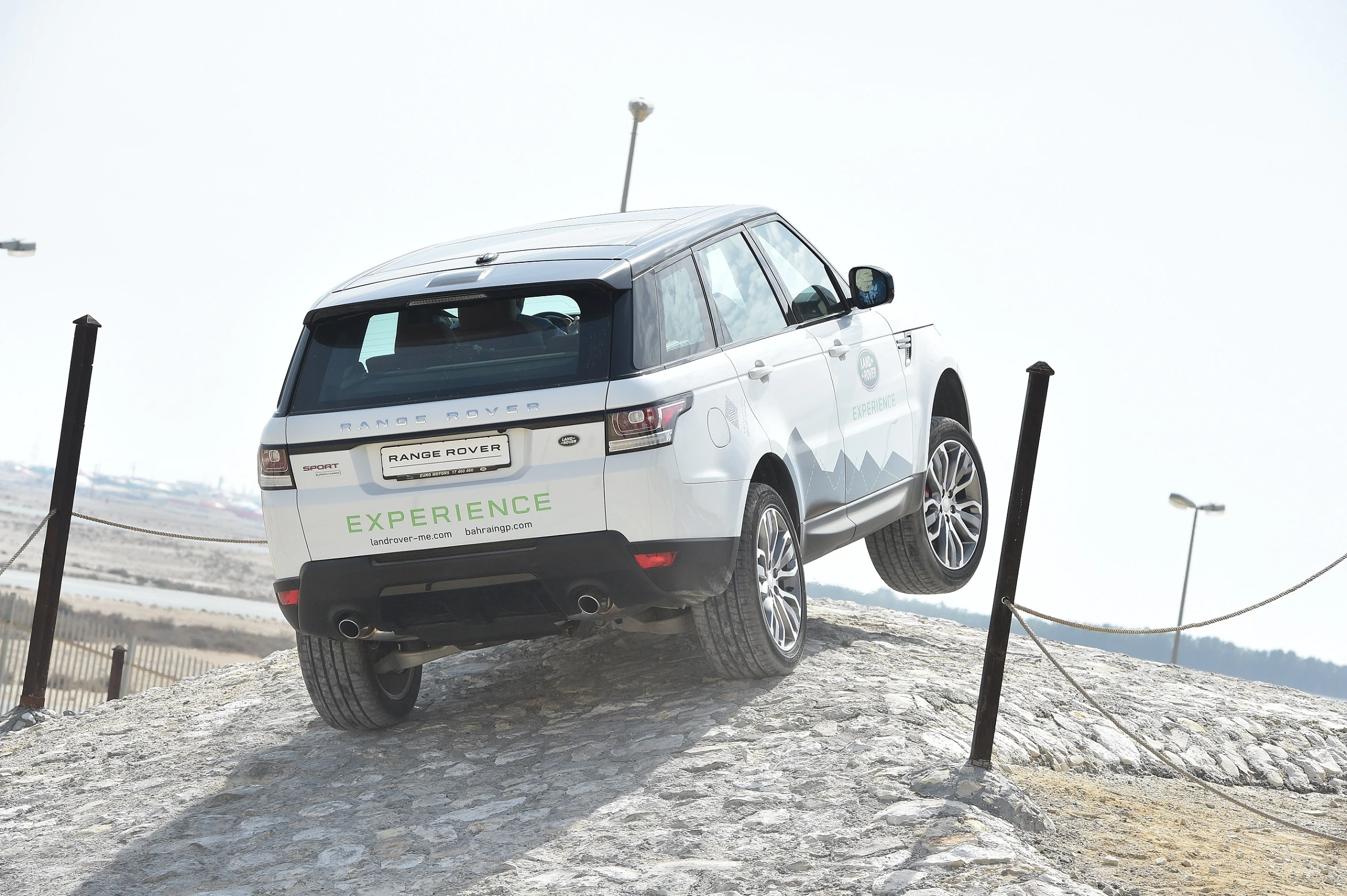 Ein weißer Range Rover fährt auf einer steinigen, geneigten Strecke mit einem Rad in der Luft.