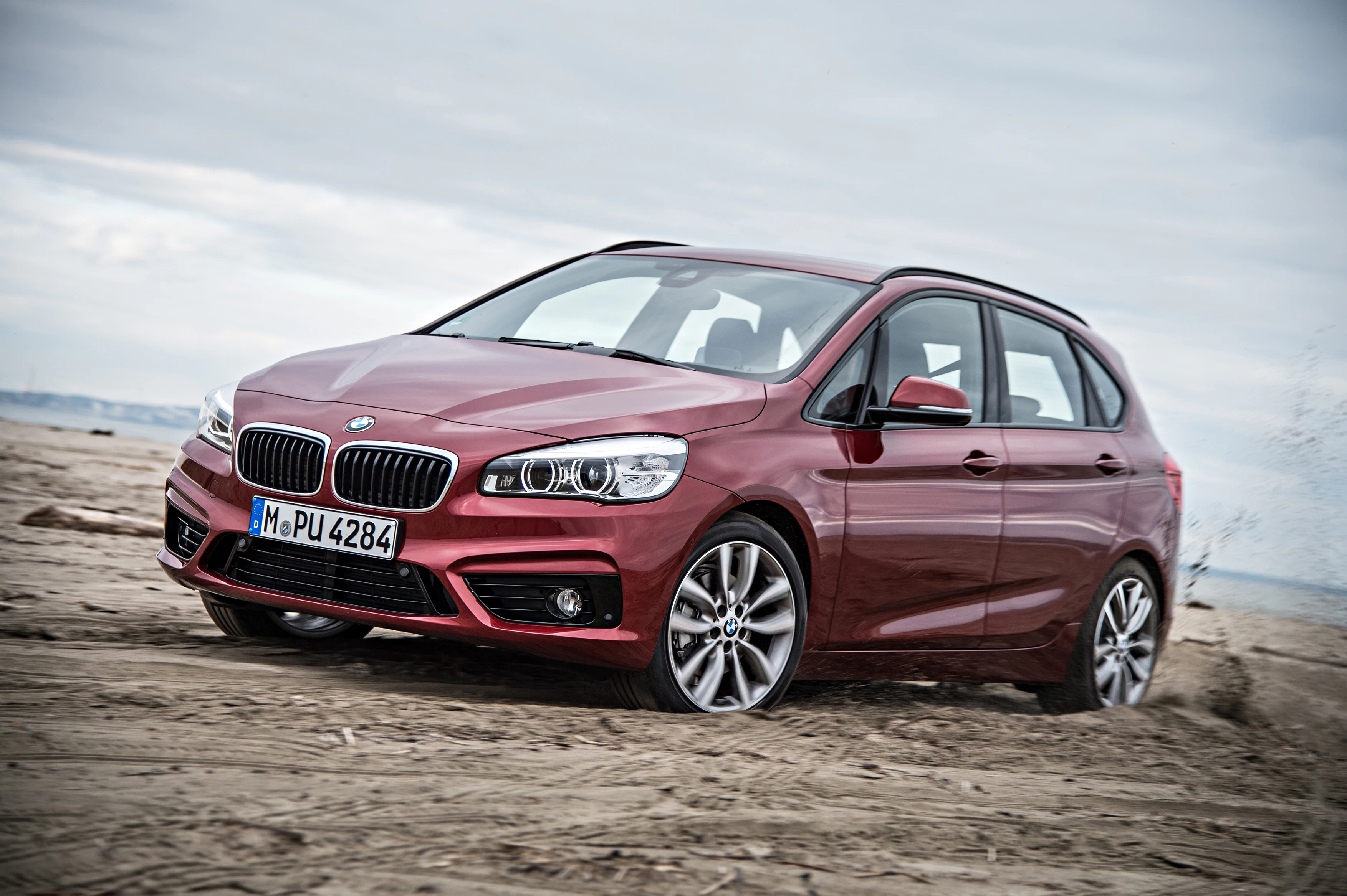 Roter BMW auf sandigem Gelände vor einem bewölkten Himmel, seitlich von vorne fotografiert.