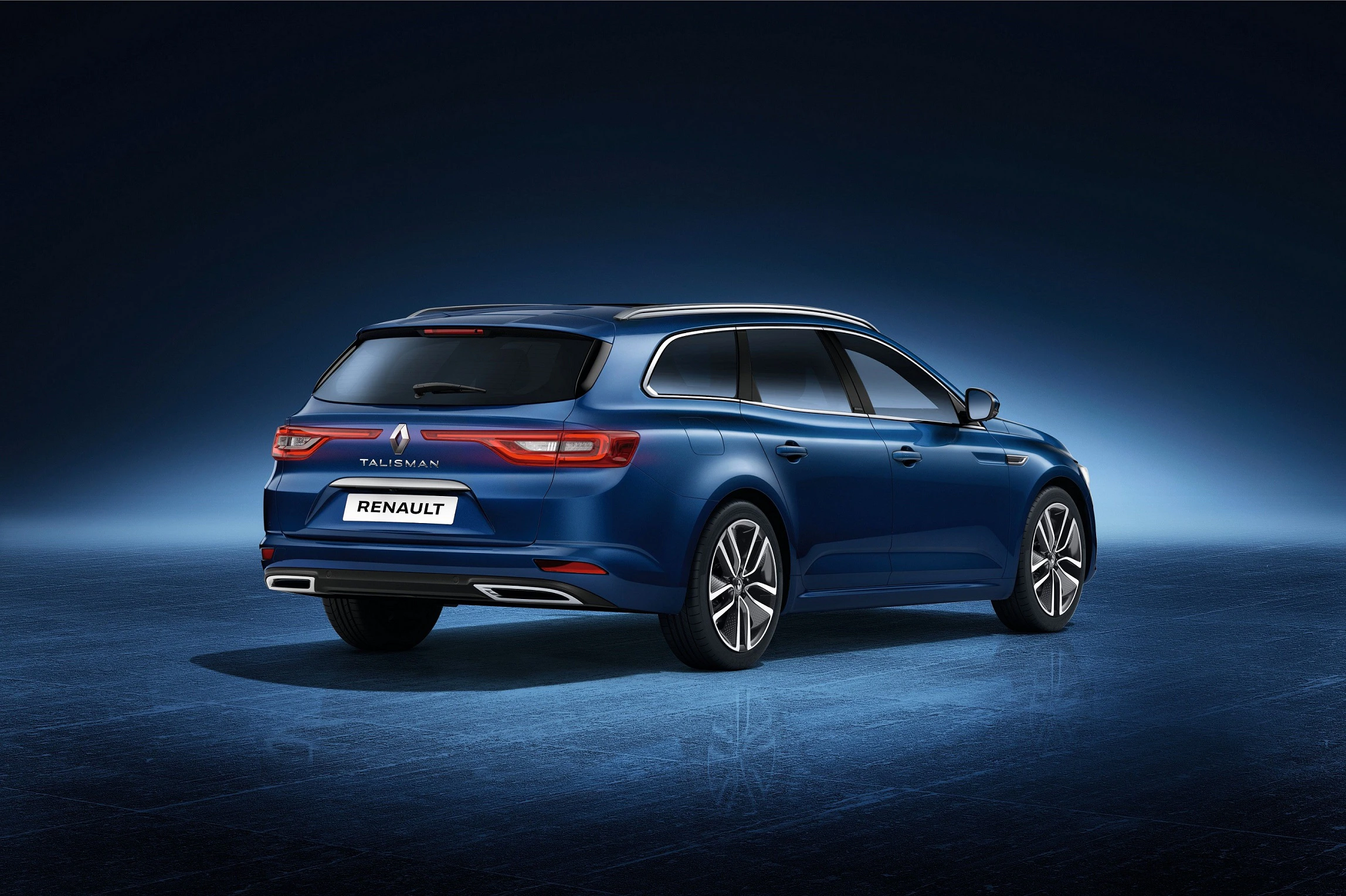 Blauer Renault Talisman Kombi vor einem dunklen, beleuchteten Hintergrund, Heck und rechte Seite sichtbar.