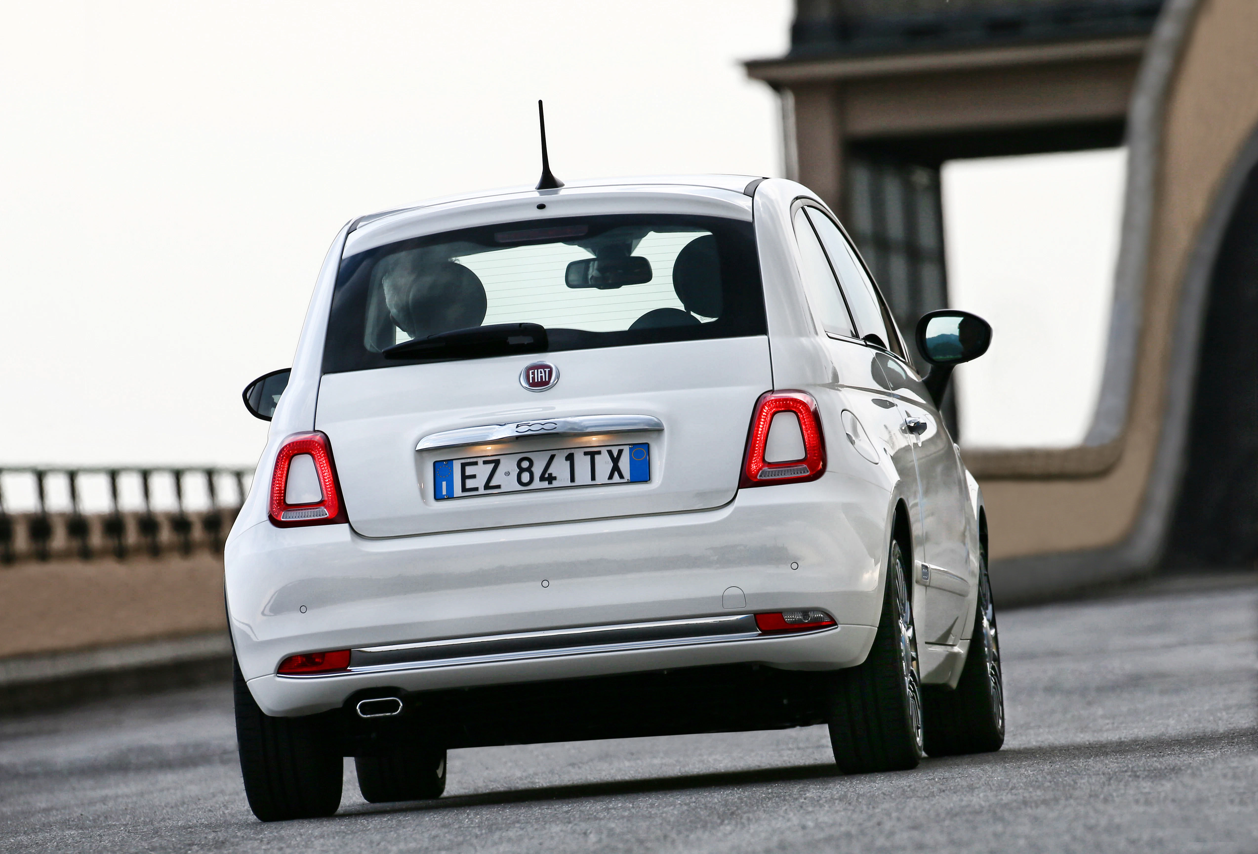 Ein weißer Fiat 500 fährt auf einer kurvigen Straße. Er ist von hinten sichtbar mit italienischem Kennzeichen.
