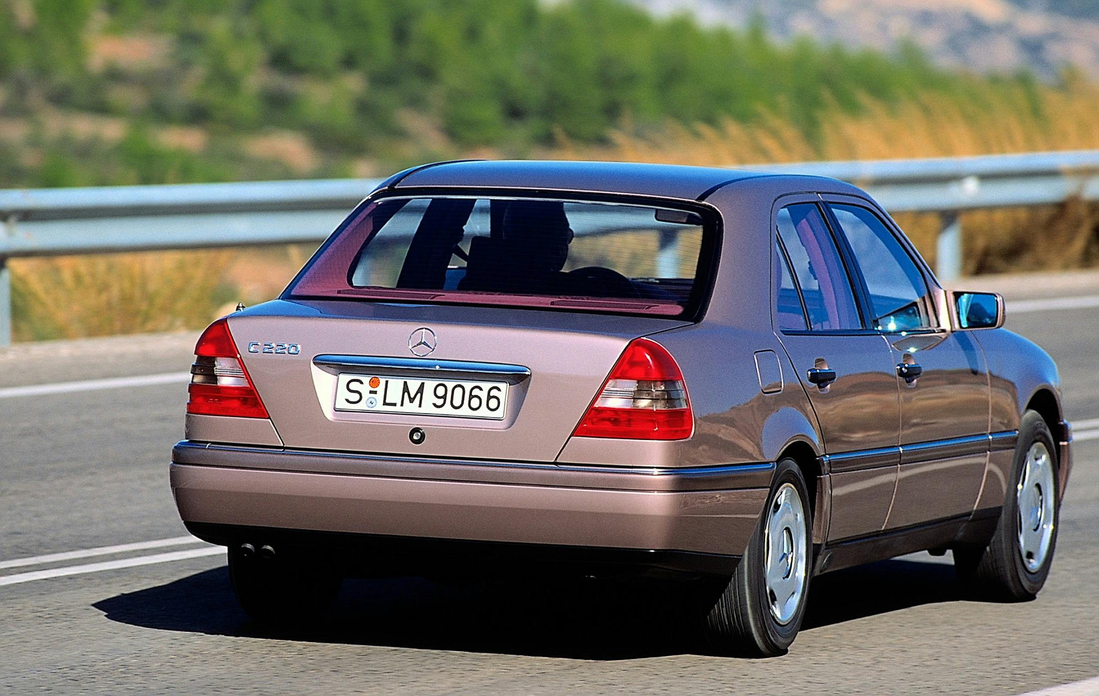 Silberner Mercedes-Benz E-Klasse von hinten auf einer Landstraße, mit grüner Landschaft im Hintergrund.