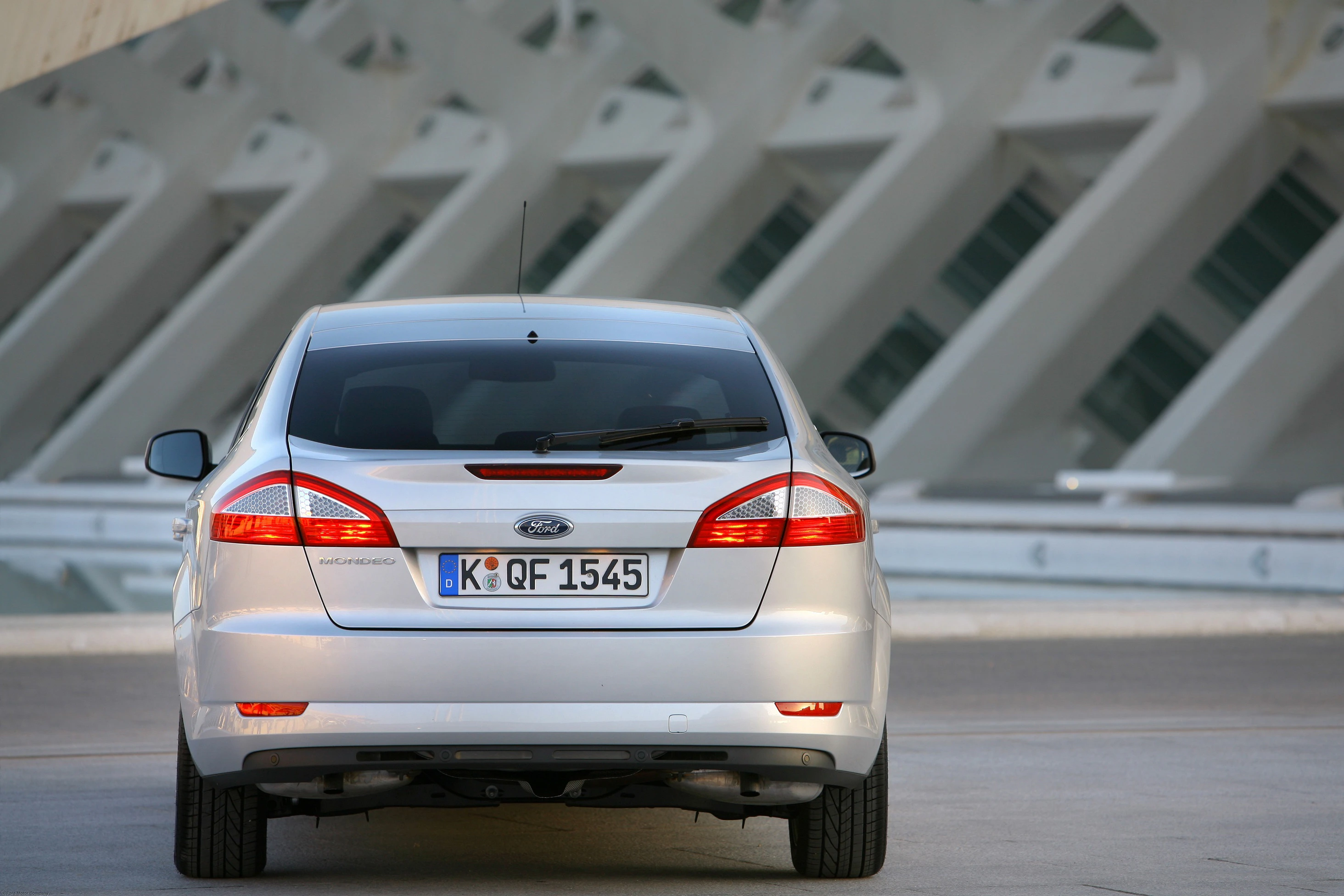 Silberner Ford Mondeo vor moderner Architektur, von hinten fotografiert, mit Kölner Kennzeichen auf einer asphaltierten Fläche.