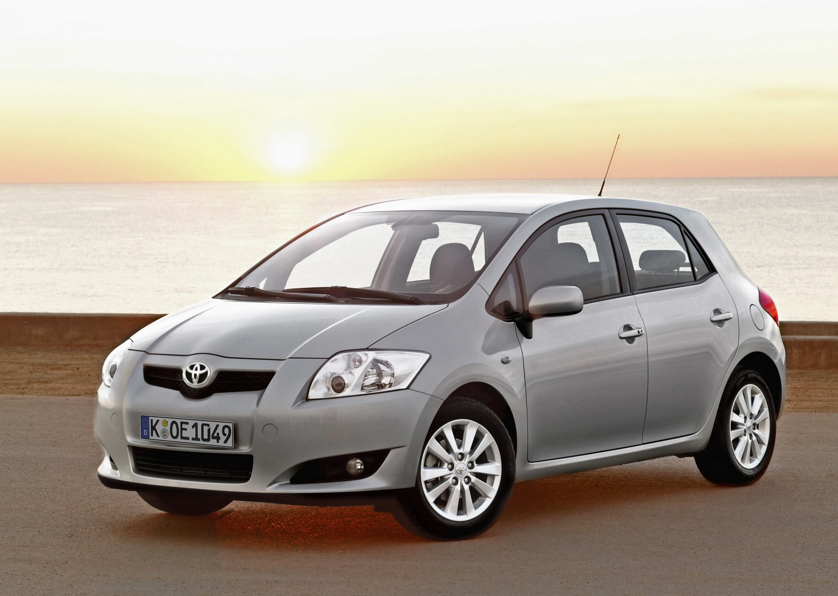 Silberner Toyota Kleinwagen steht auf einer Straße mit Meer im Hintergrund bei Sonnenuntergang.