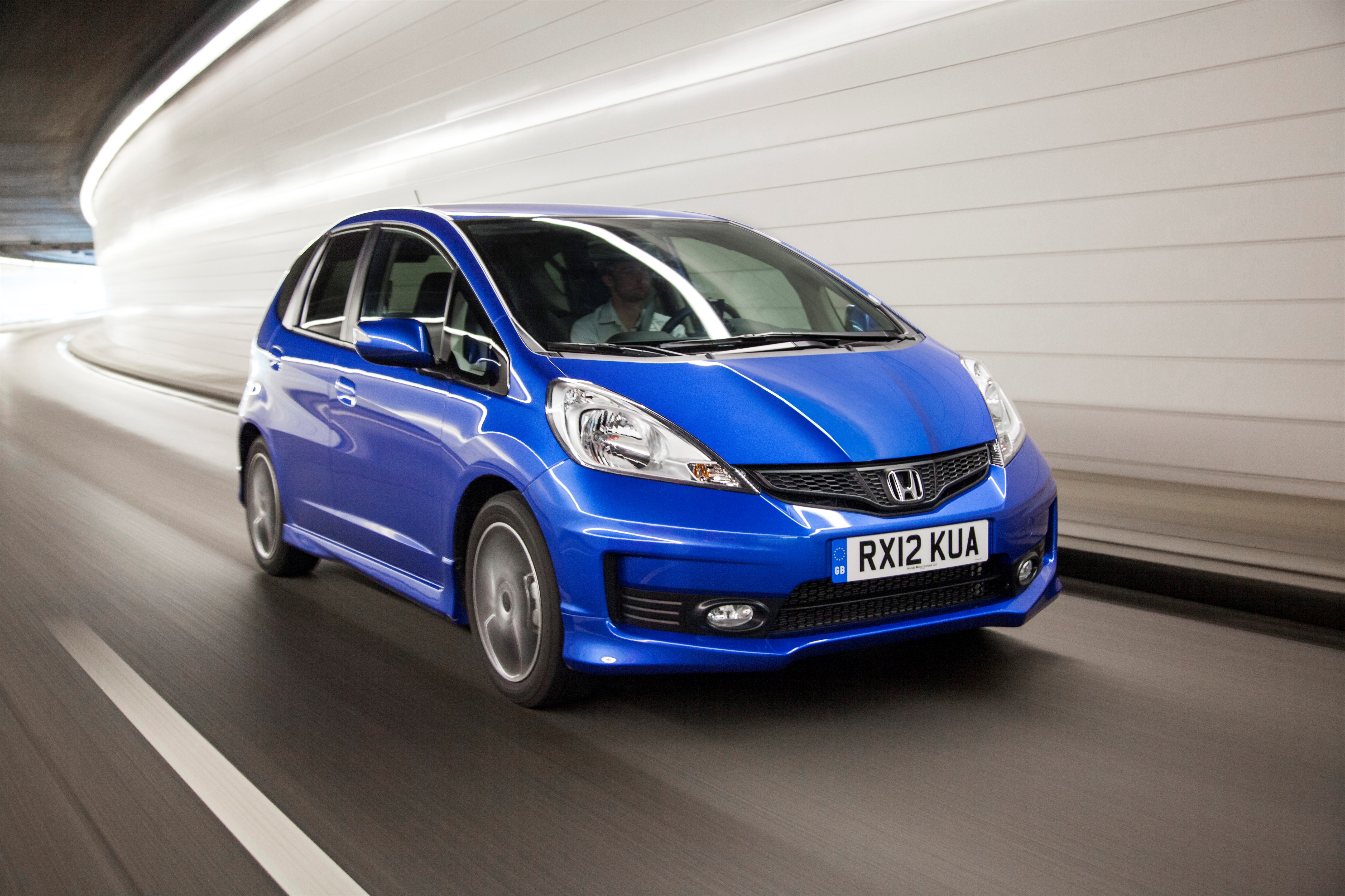 Blauer Honda Jazz fährt mit Bewegungsunschärfe durch einen hell erleuchteten, gekrümmten Tunnel.