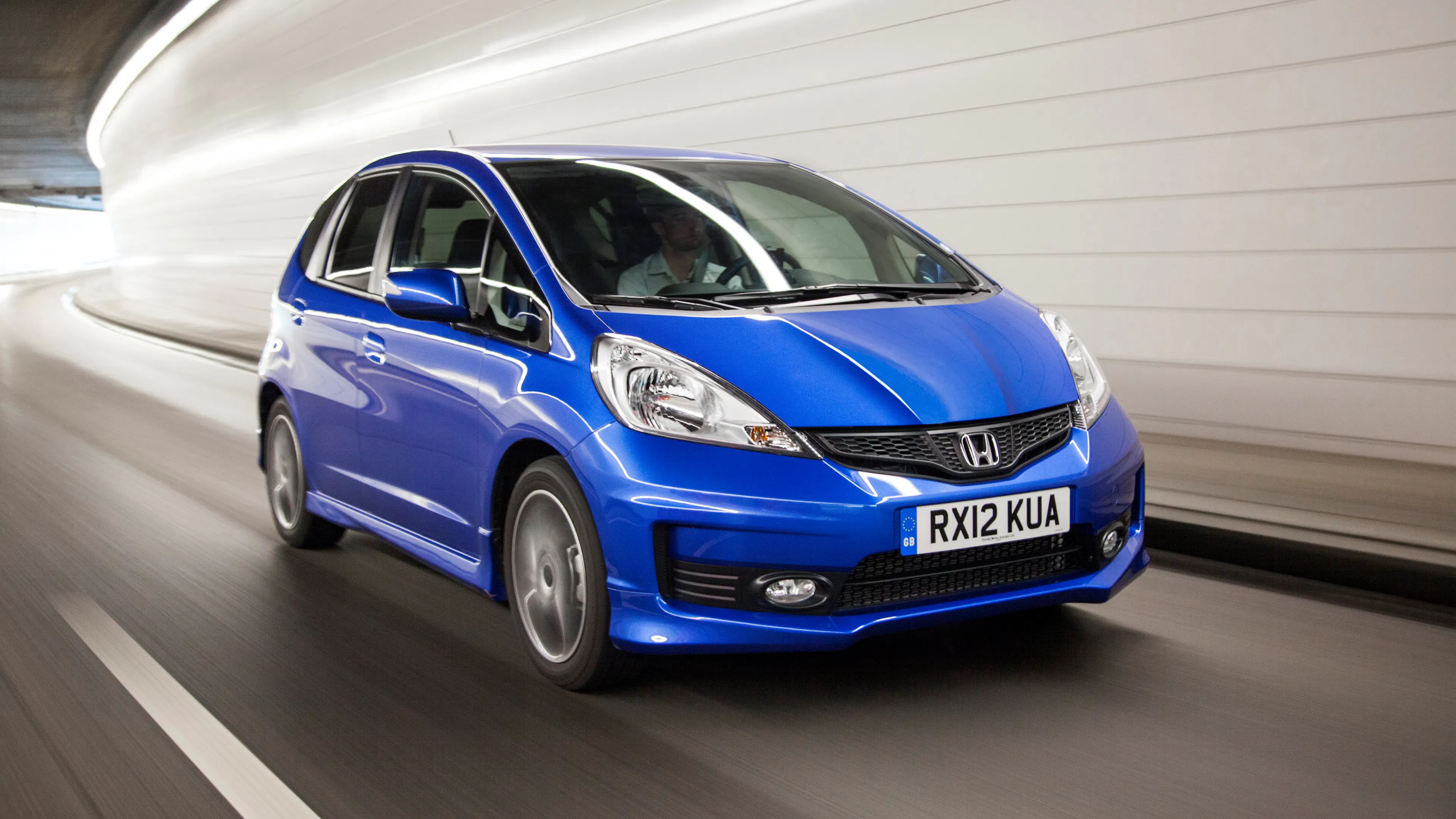 Blauer Honda Jazz fährt mit Bewegungsunschärfe durch einen hell erleuchteten, gekrümmten Tunnel.