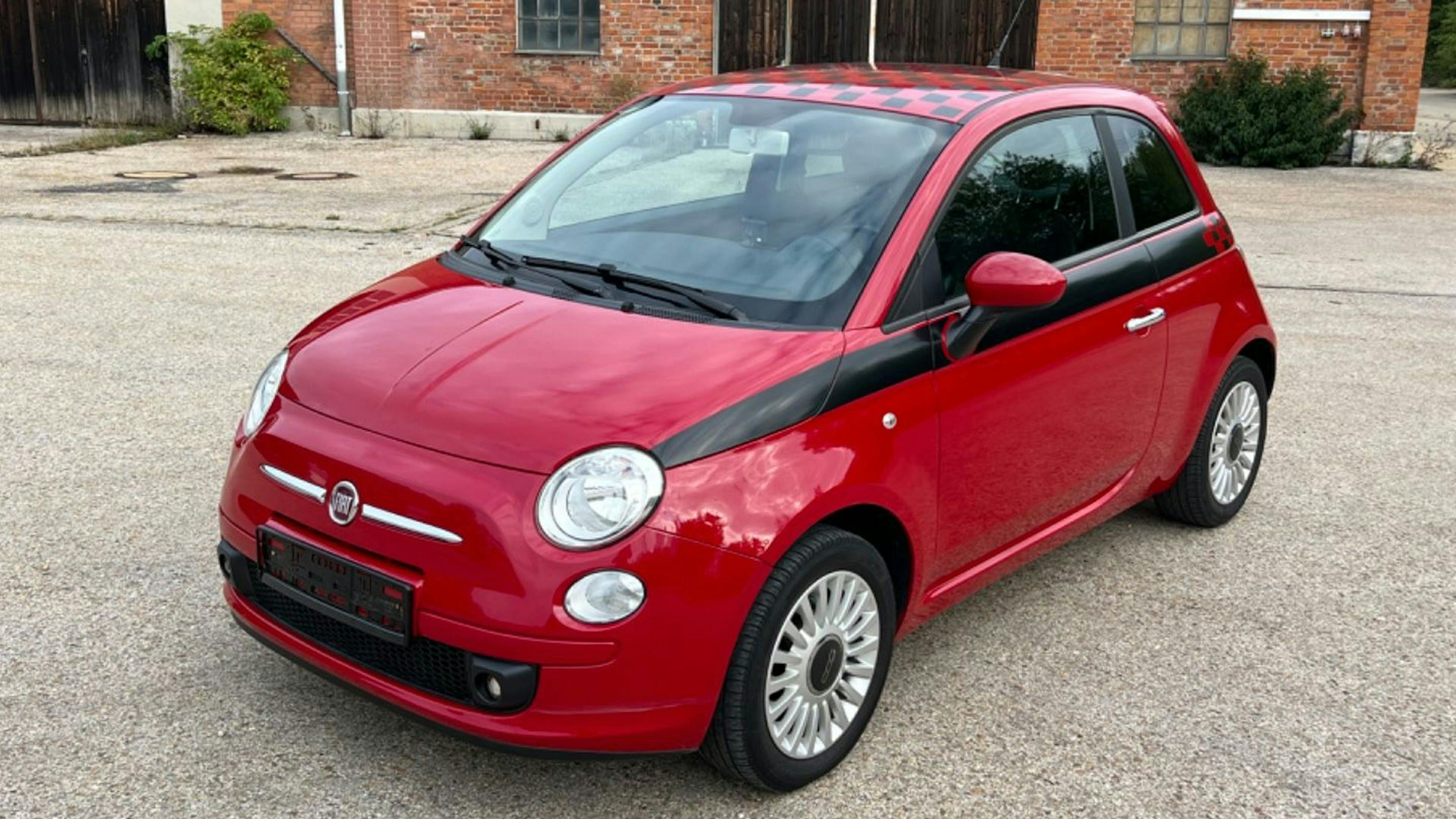 Ein roter Fiat 500 Kleinstwagen steht vor einem Haus mit Backsteinfassade.