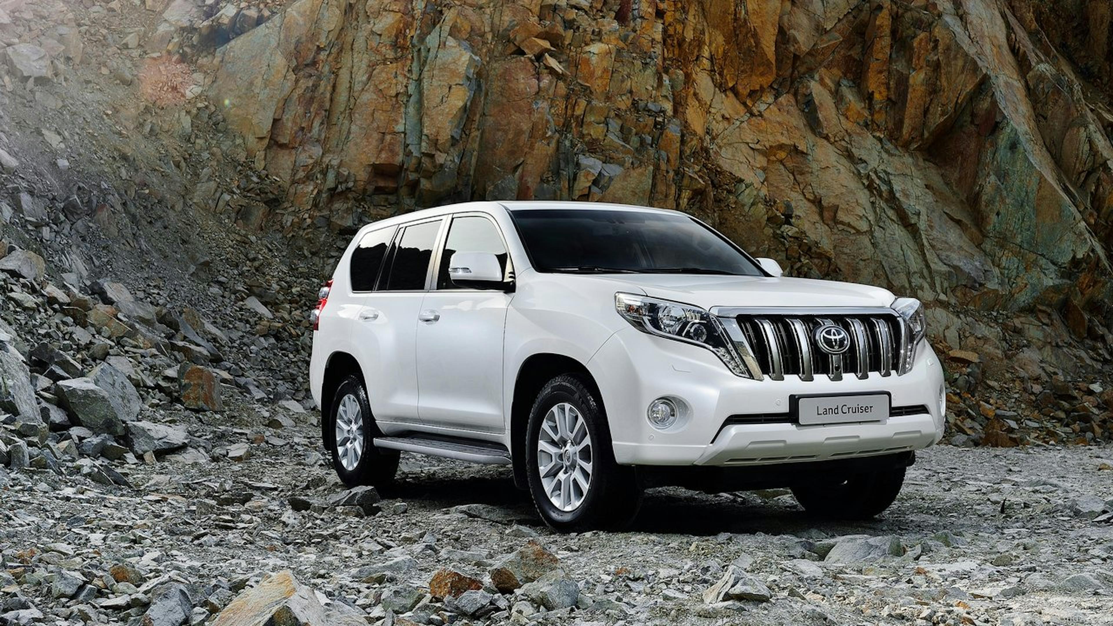 A white Toyota Land Cruiser is parked on a slope next to rubble.