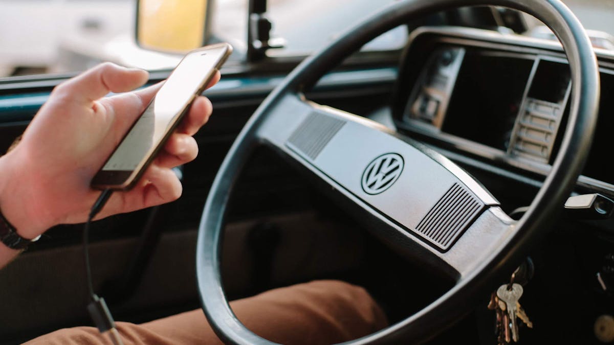 Eine Person sitzt am Steuer eines VW und bedient ein Smartphone