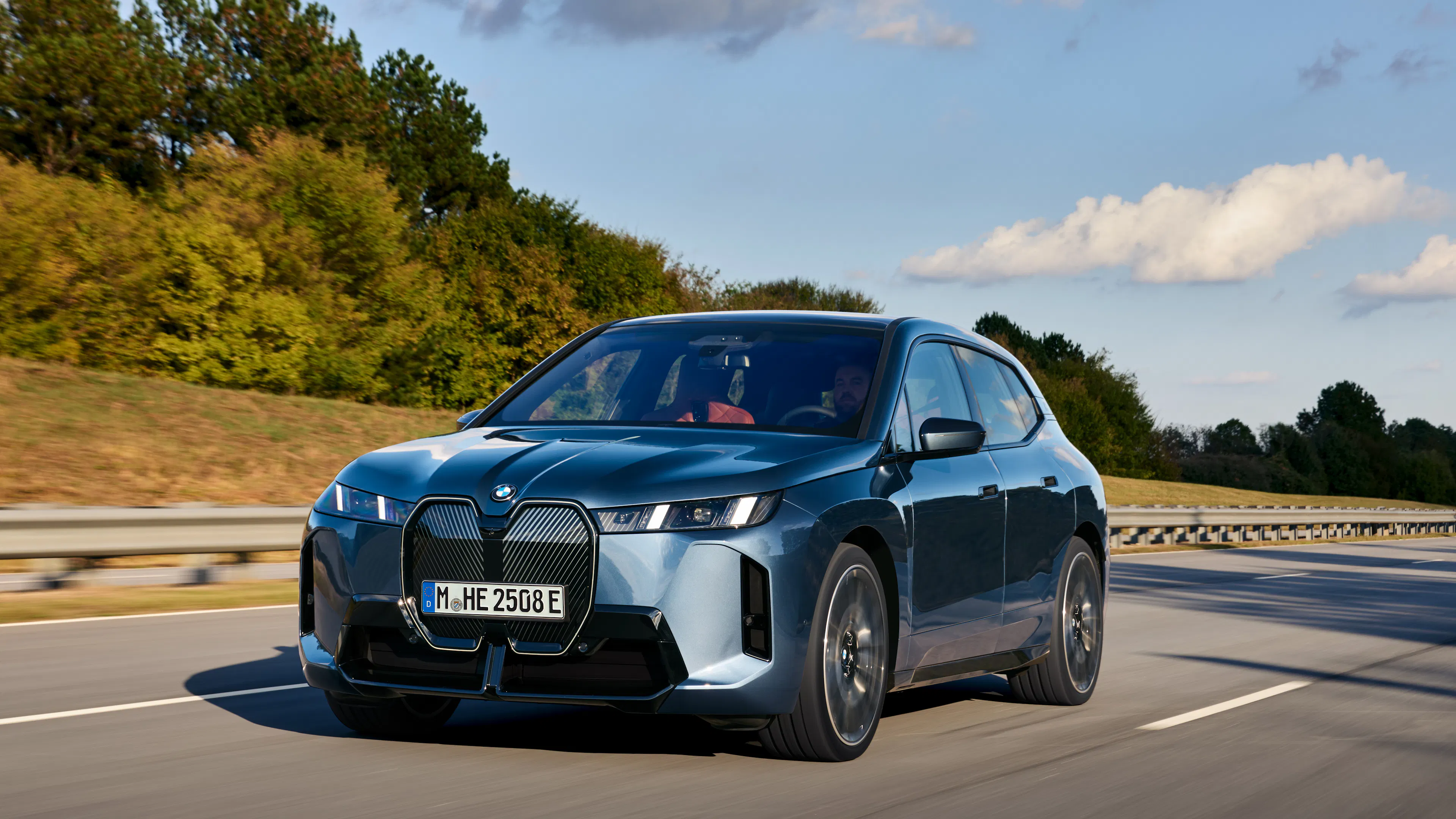 Ein dunkelblauer BMW iX fährt auf einer Landstraße.