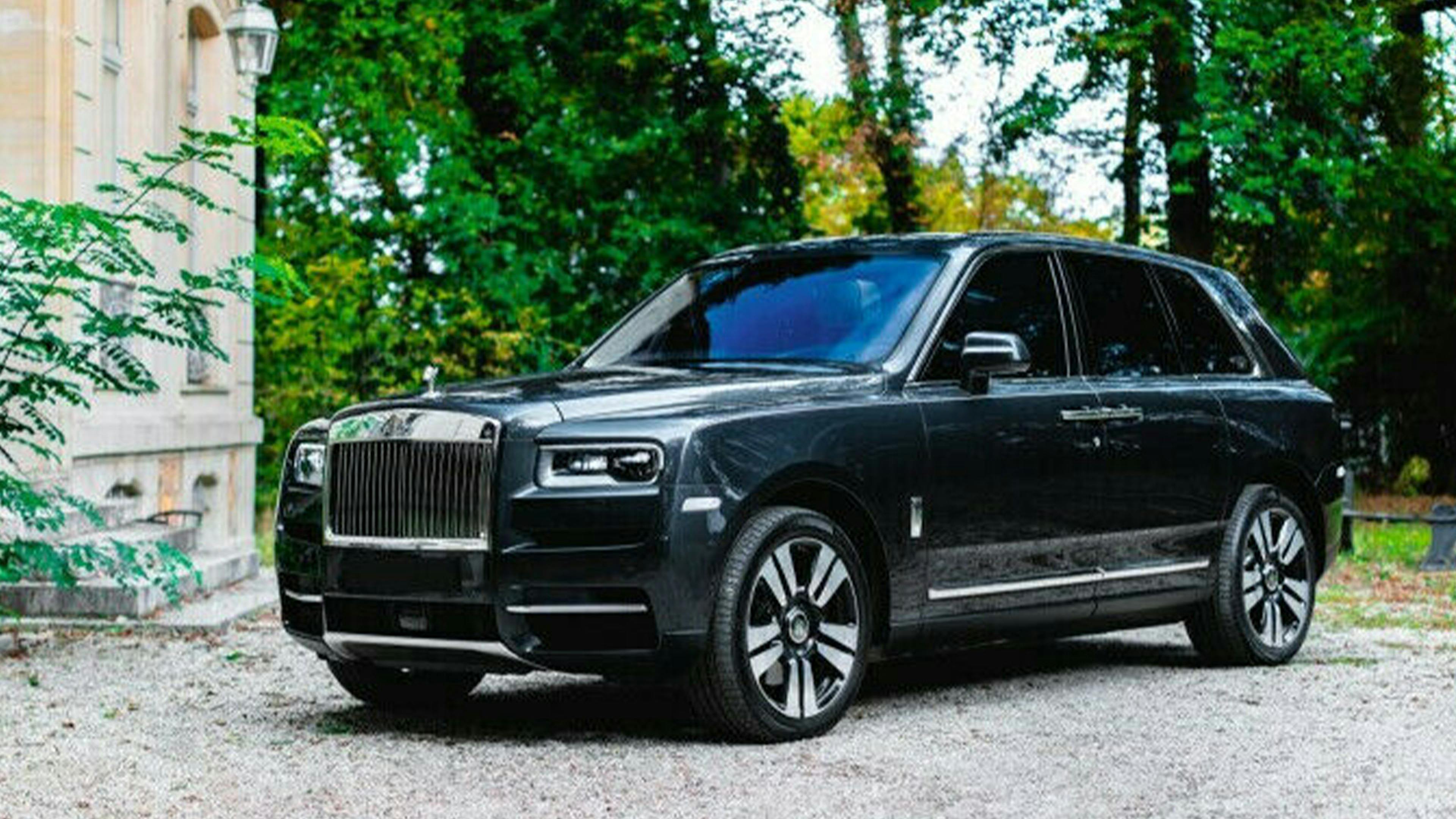 Ein schwarzer Rolls-Royce Cullinan steht vor einem hellen Gebäude mit Bäumen im Hintergrund.