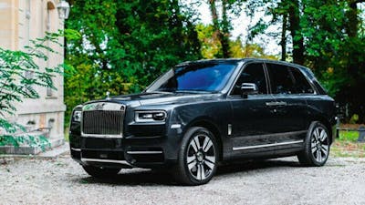 Ein schwarzer Rolls-Royce Cullinan steht vor einem hellen Gebäude mit Bäumen im Hintergrund.