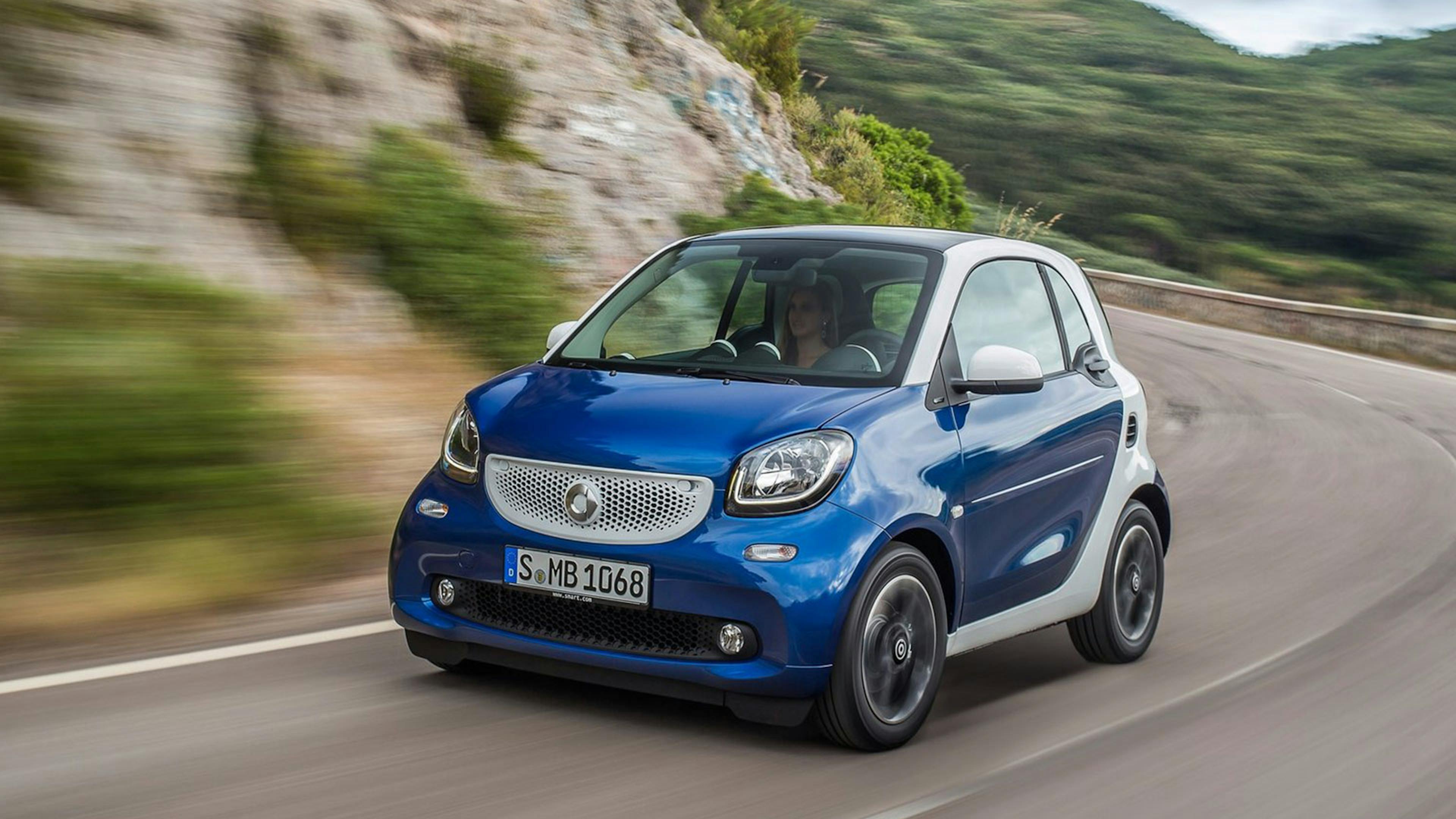 Ein blauer Smart Fortwo Kleinstwagen fährt eine kurvige Bergstraße entlang.