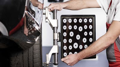 Ein Mechaniker bereitet eine Achsvermessung an einem schwarzen Pkw vor.