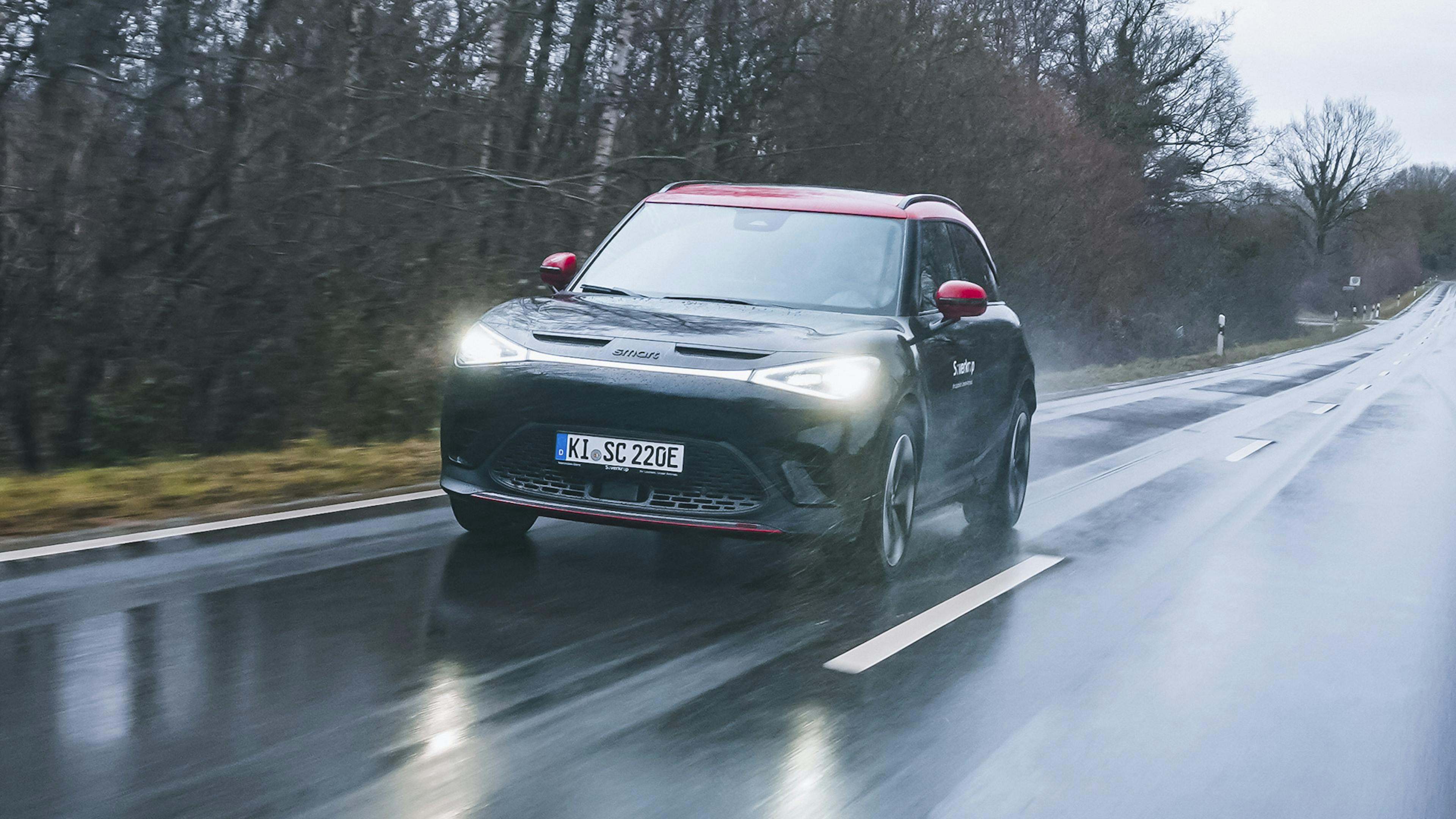Ein schwarz-roter Smart #1 Brabus fährt im Regen über eine Landstraße.
