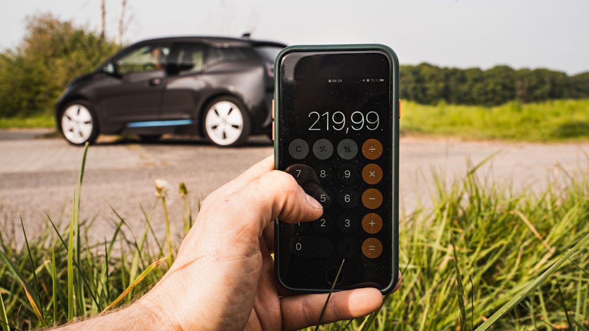 Ein Handy mit Taschenrechner im Vordergrund vor einem BMW am Feldrand