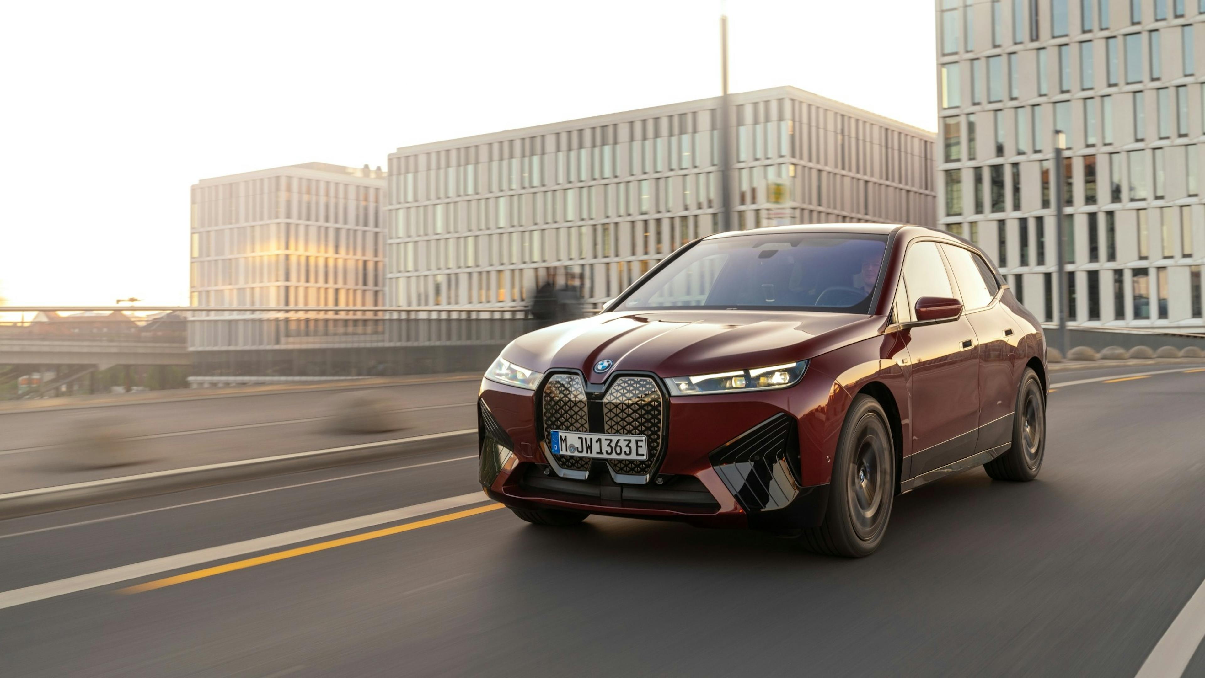 A red BMW iX drives through a city in the evening.