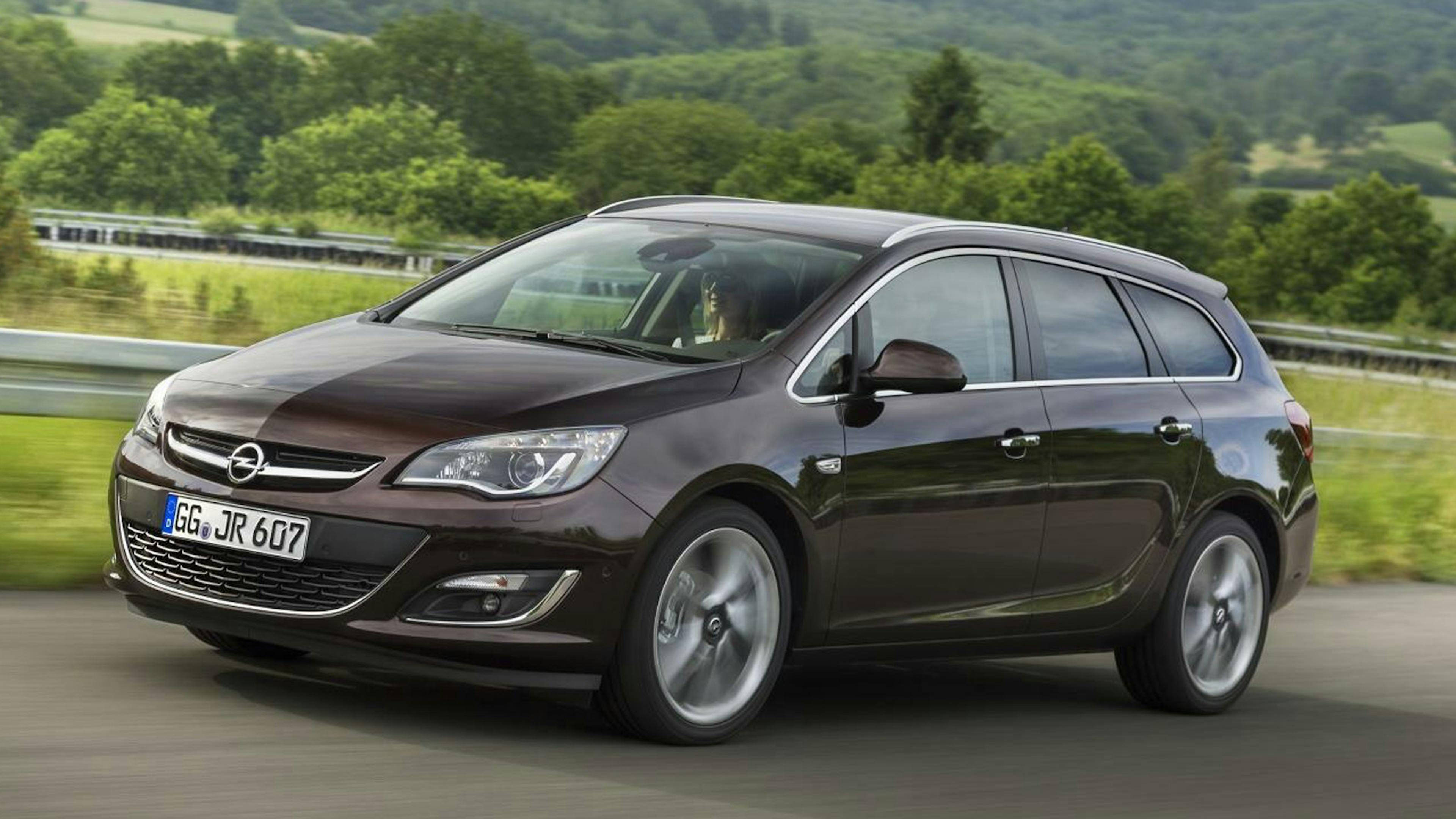 Ein dunkler Opel Astra J Sports Tourer-Kombi fährt eine Landstraße entlang.