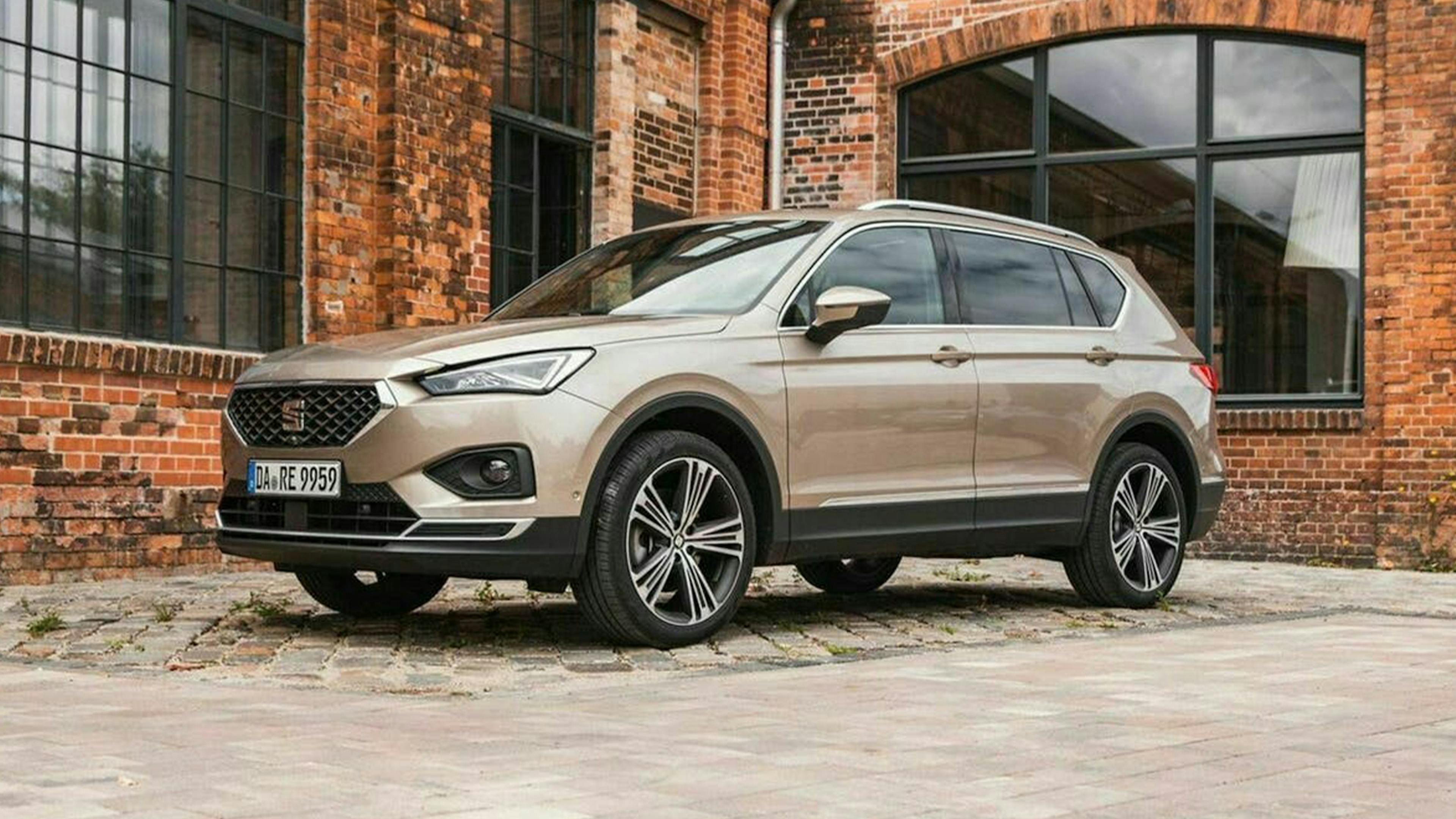 Ein hellbrauner Seat Tarraco 1.5 TSI steht vor einem Backsteingebäude