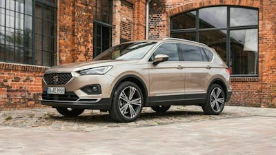 Ein hellbrauner Seat Tarraco 1.5 TSI steht vor einem Backsteingebäude