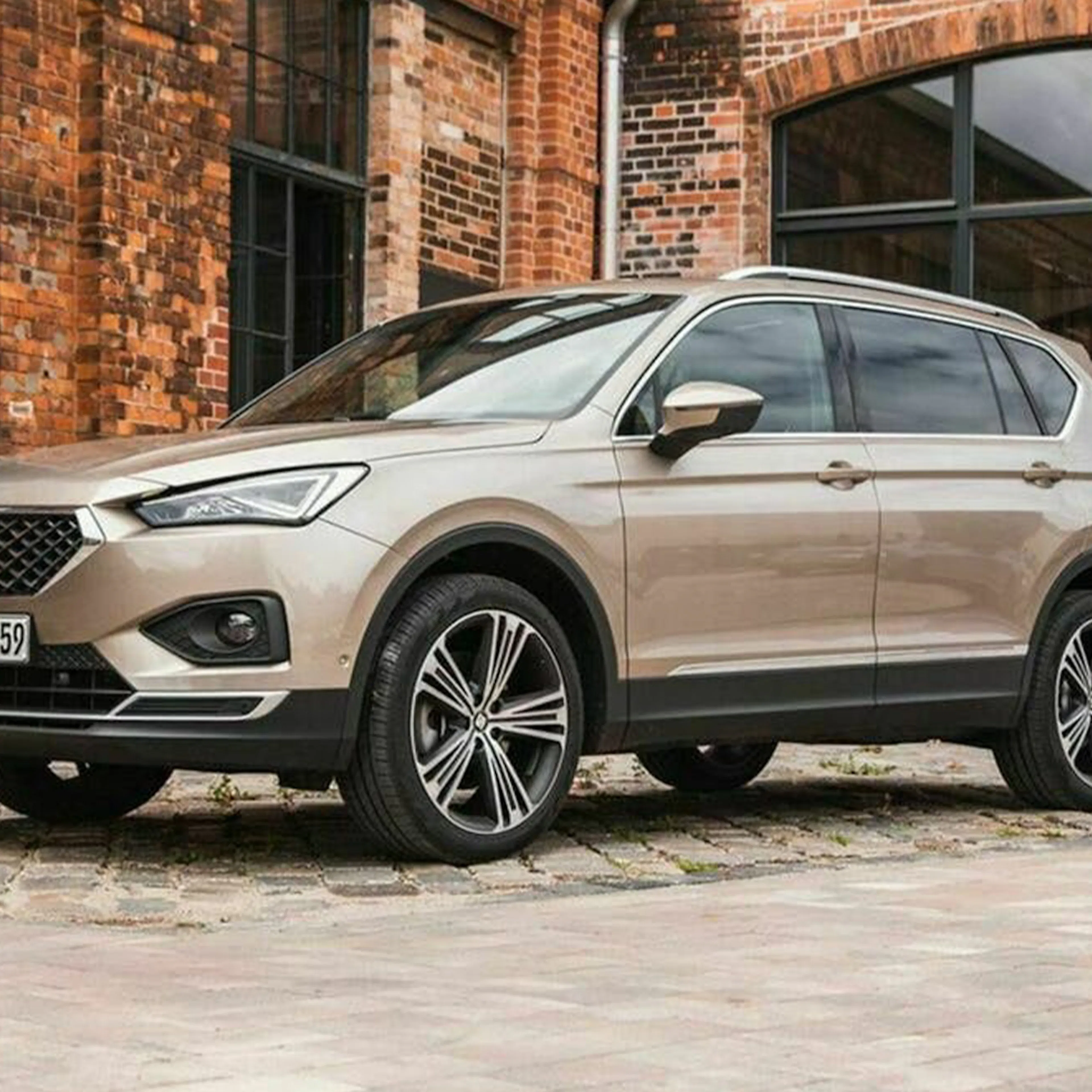 Ein hellbrauner Seat Tarraco 1.5 TSI steht vor einem Backsteingebäude