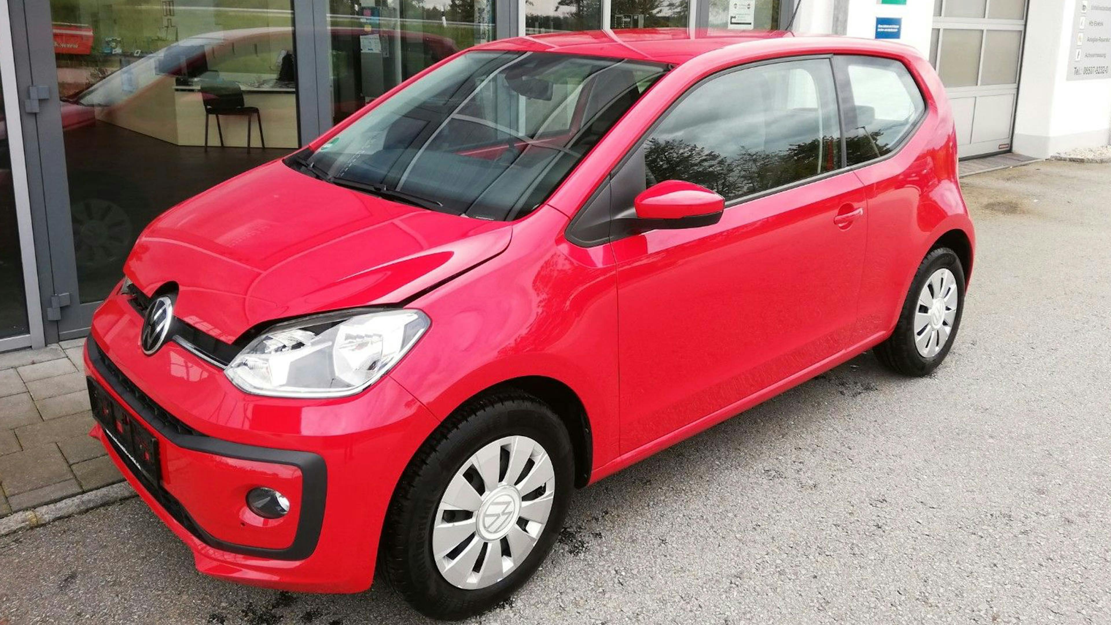Ein roter VW Eco up! steht vor einem Gebäude mit Fensterfront.