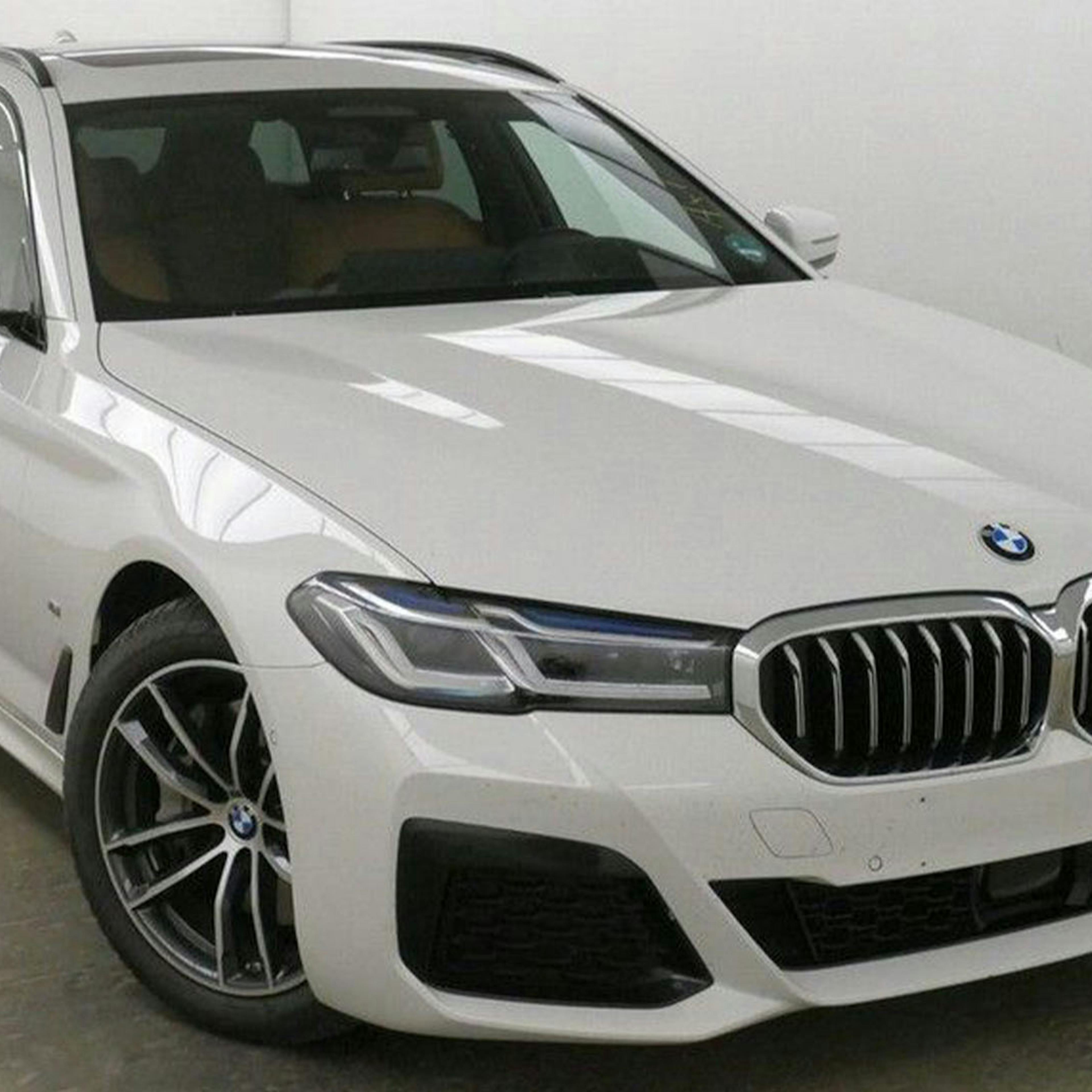 Ein weißer BMW 5er Touring steht vor einer weißen Wand.