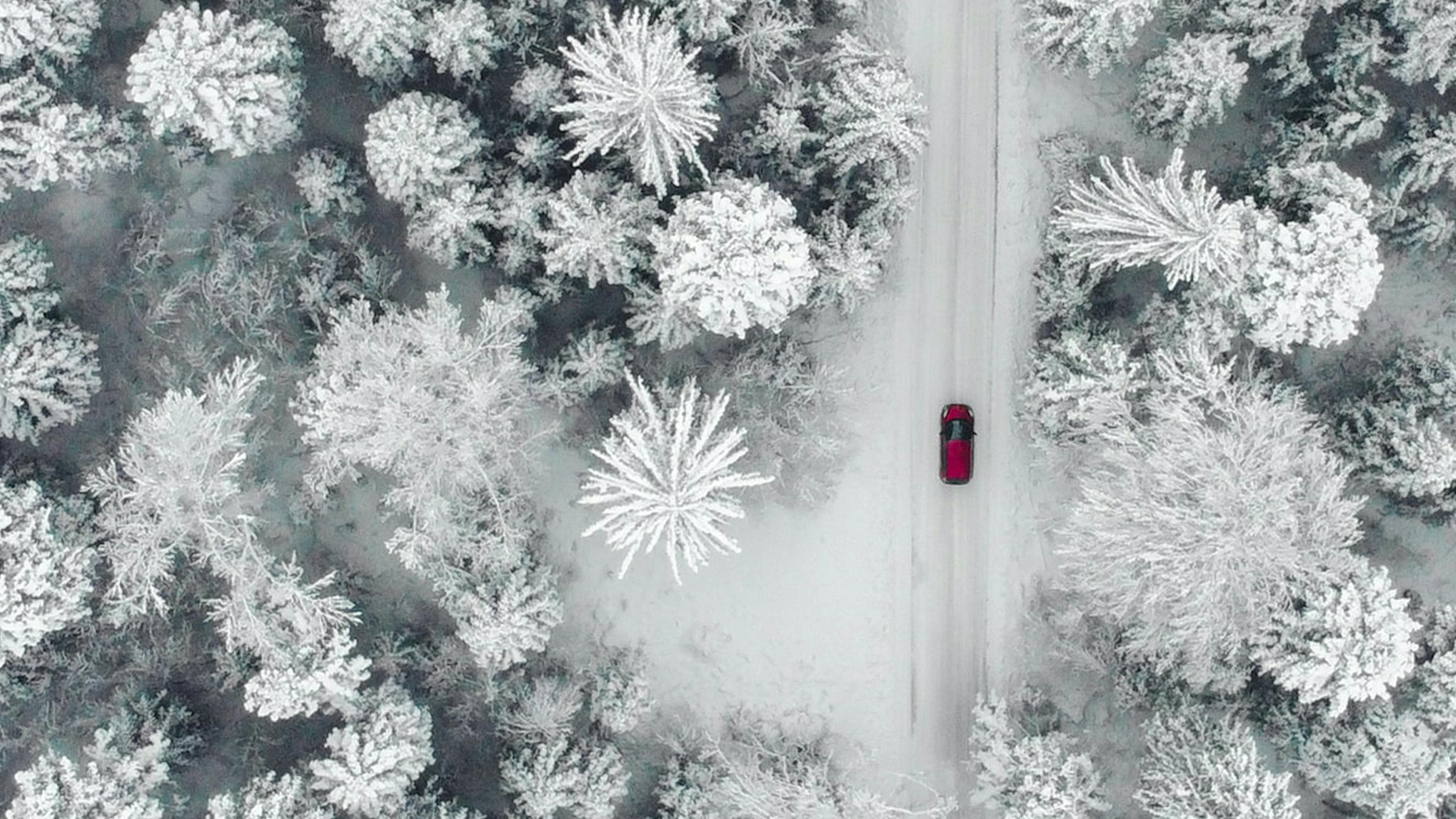 Luftaufnahme eines roten Pkw, der durch eine verschneite Landschaft fährt.
