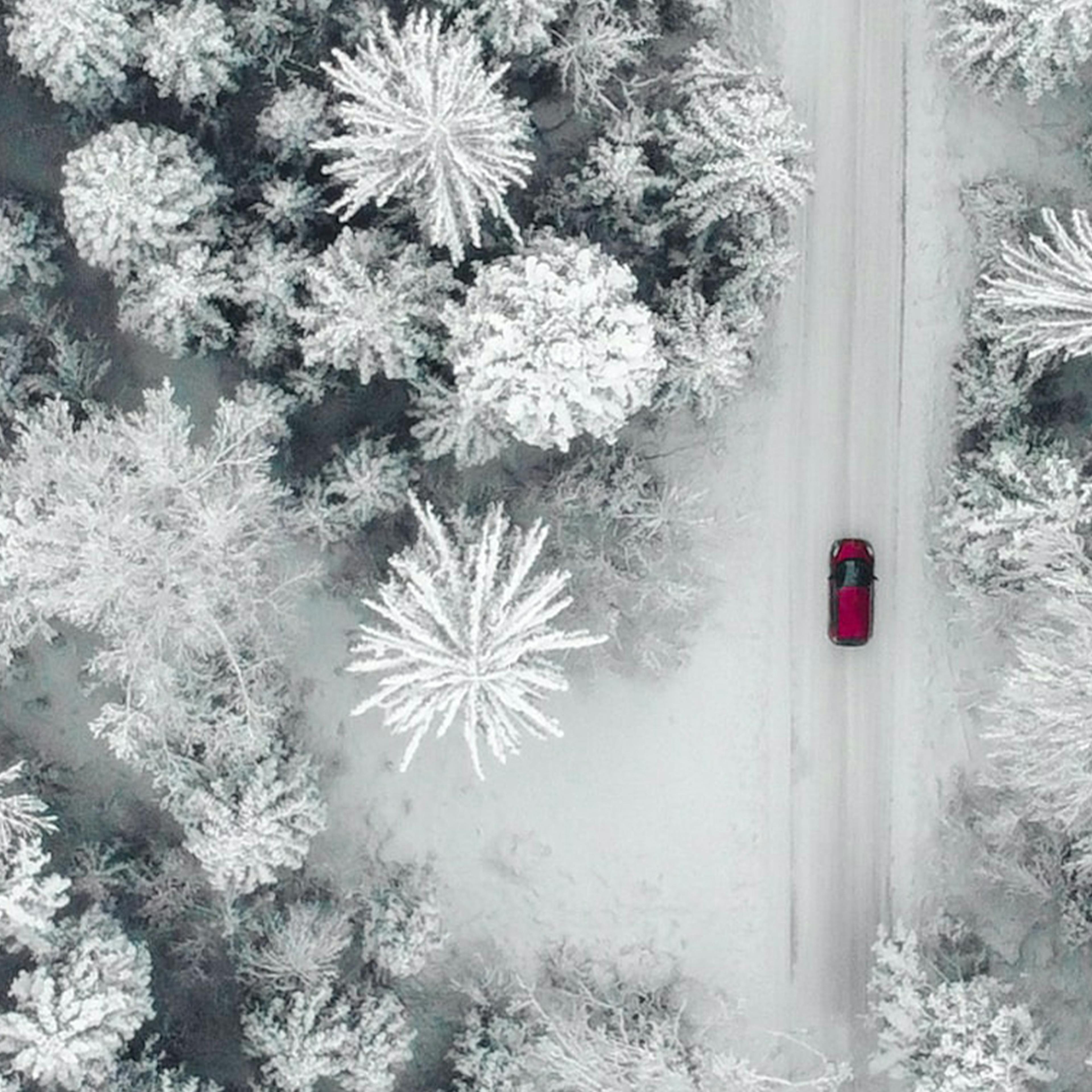 Luftaufnahme eines roten Pkw, der durch eine verschneite Landschaft fährt.