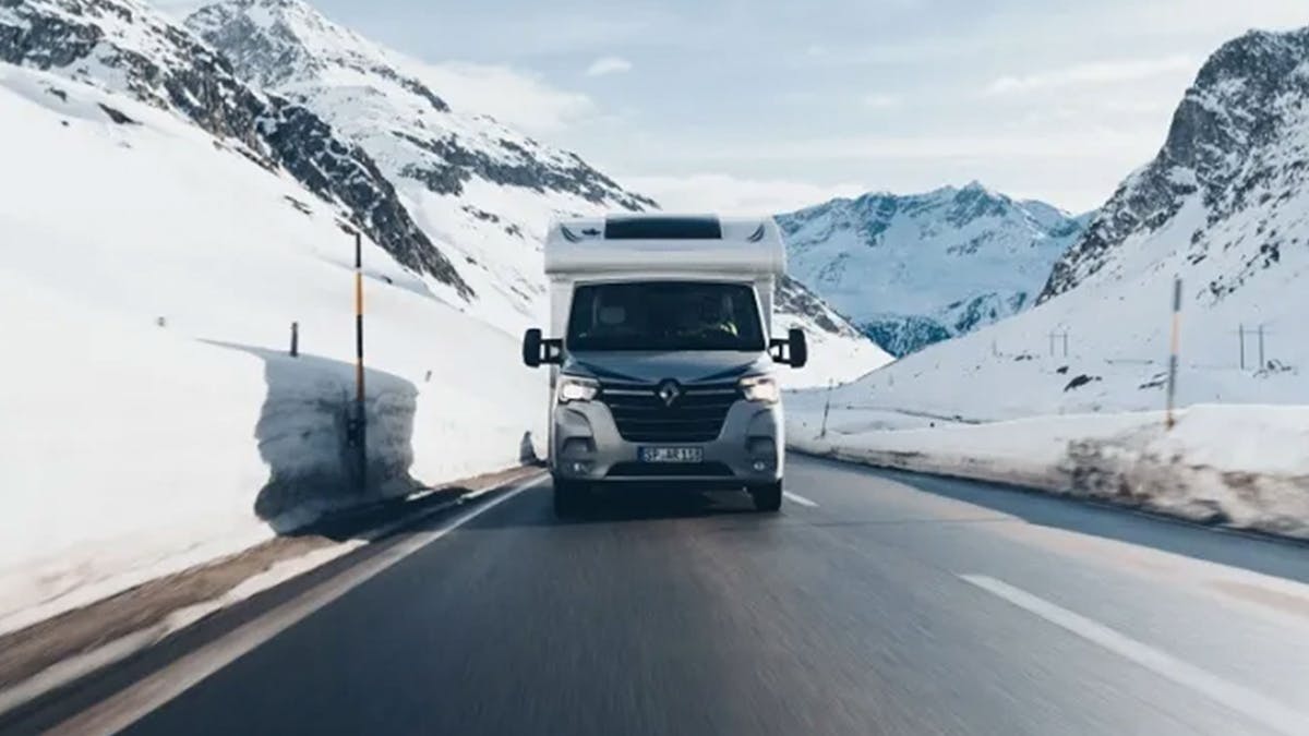 Ein Ahorn Camp T690 Wohnmobil fährt auf einer Landstraße durch eine verschneite Landschaft.